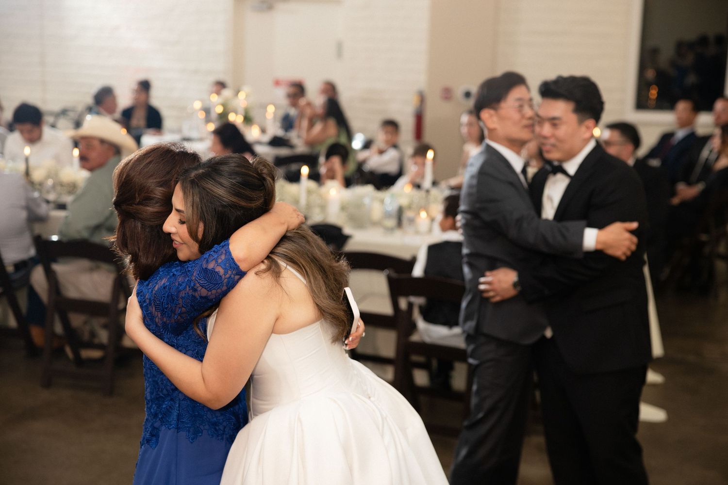 Bride shares emotional hug with mother in blue dress during parent dance at elegant wedding reception.