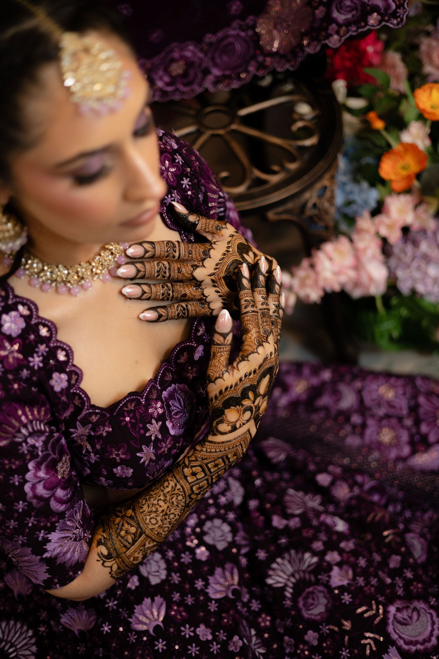 Intricate henna designs on hands surrounded by purple flowers and decorative elements.