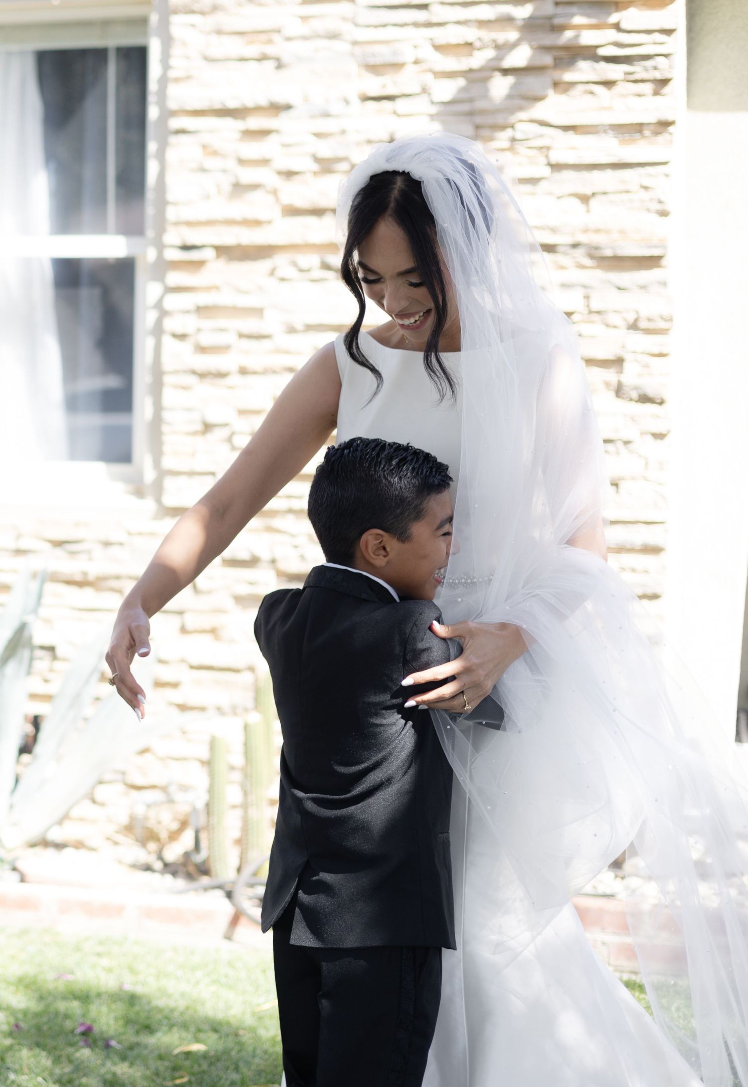 A small ring bearer in formal attire pulls on the hem of a flowing white wedding gown.