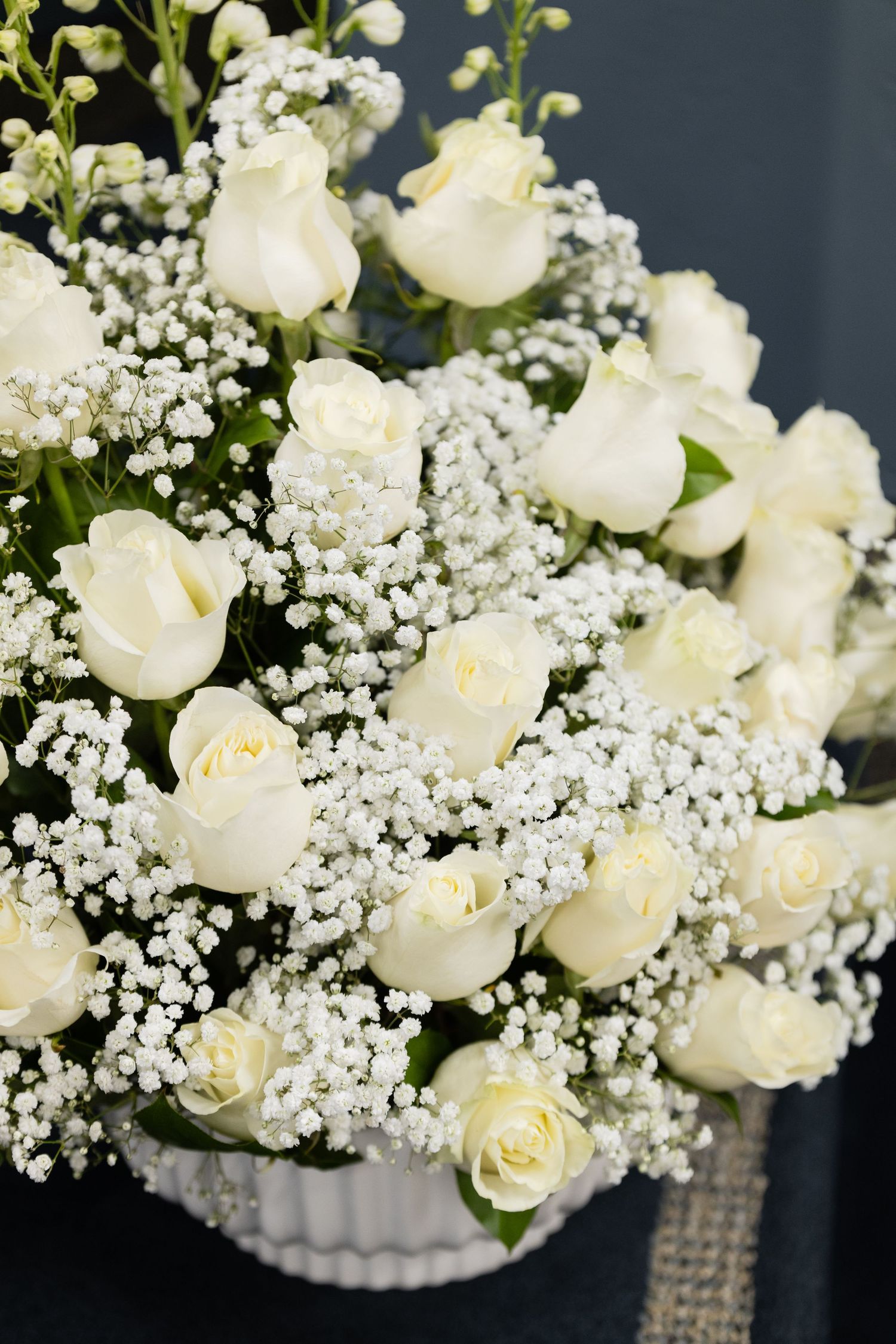 Elegant white roses and baby's breath arranged in crystal vases against a dark background.