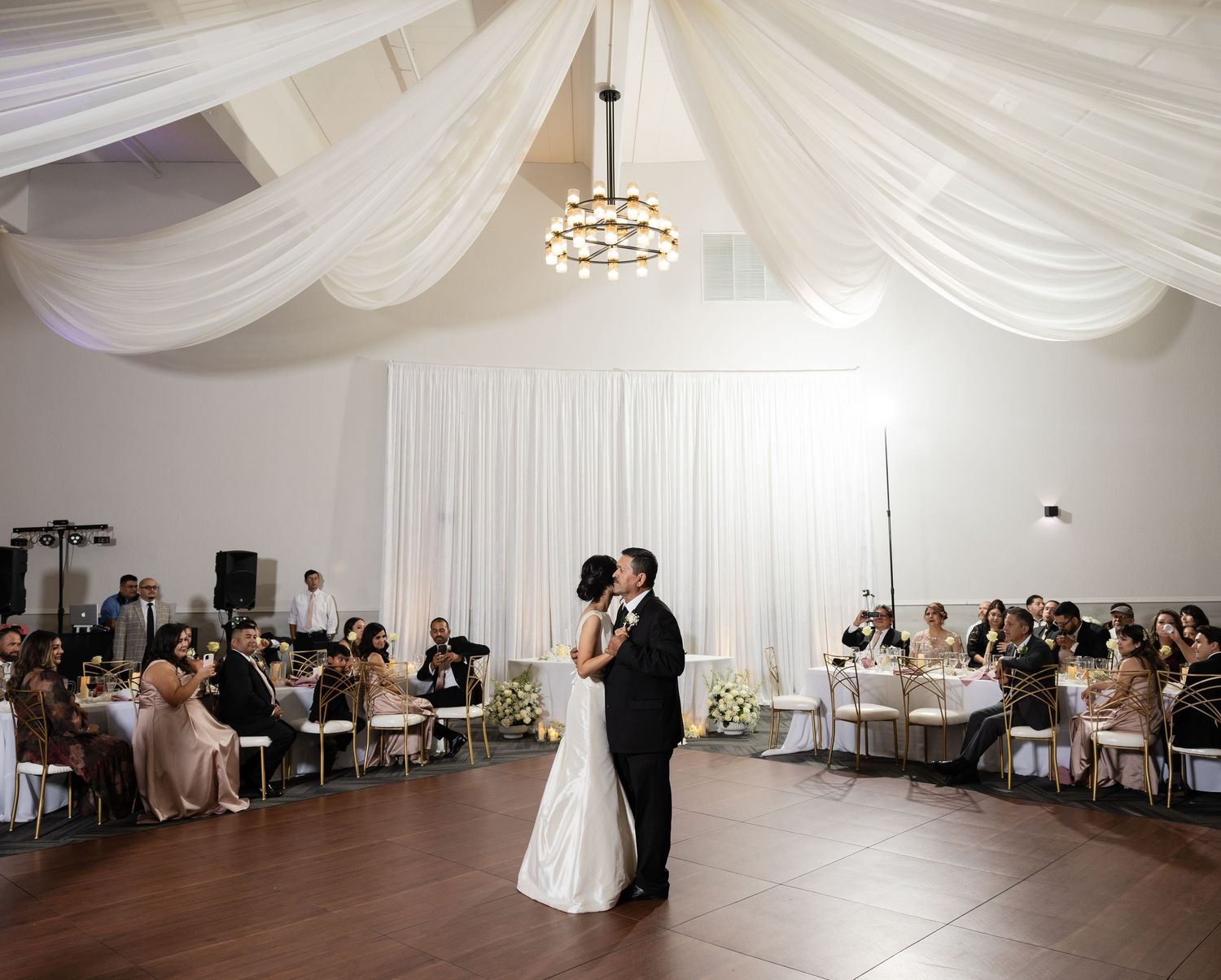 Wedding reception ballroom with white ceiling draping and modern chandeliers.