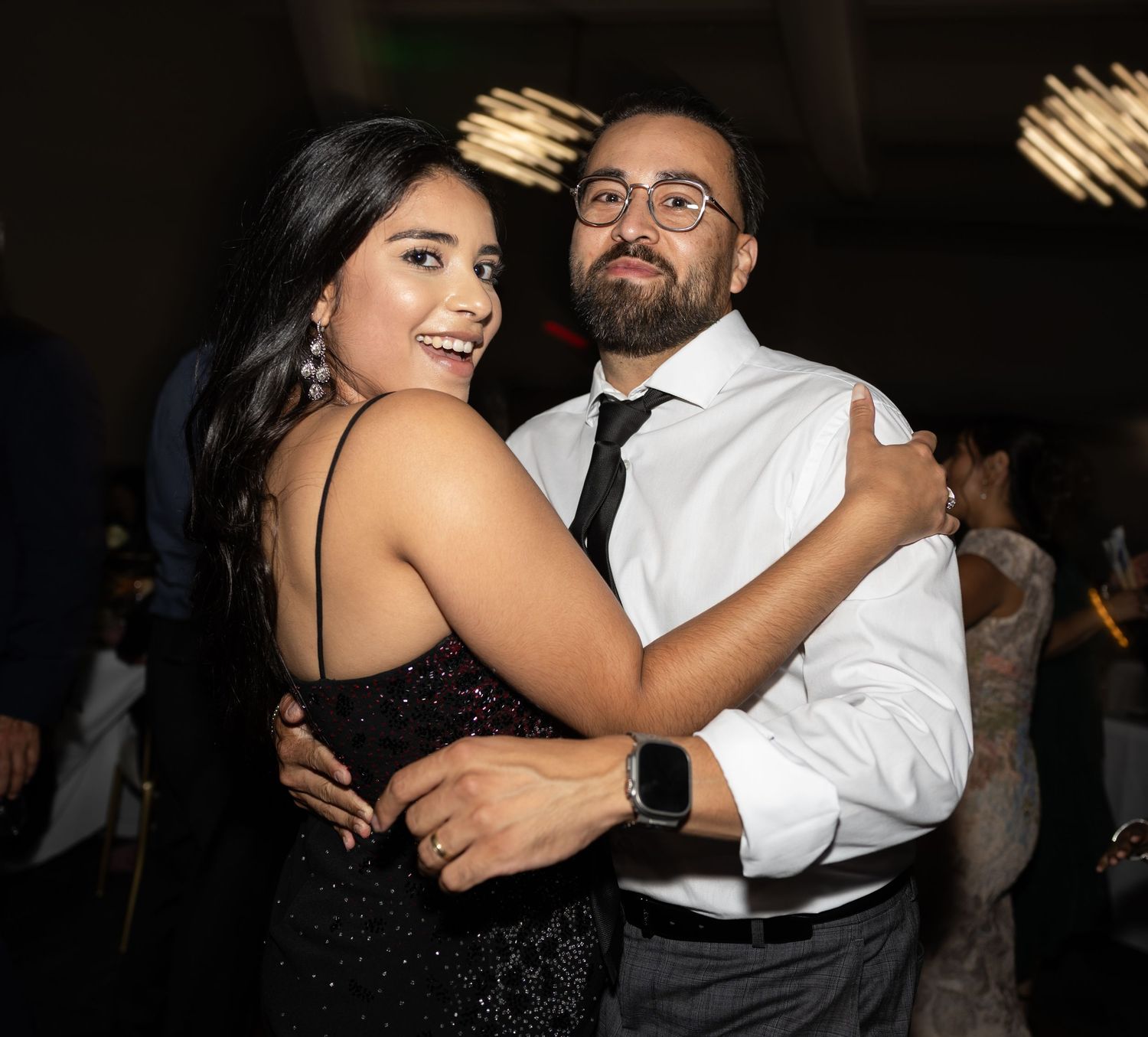 Couple dancing together at a formal event with modern lighting overhead.