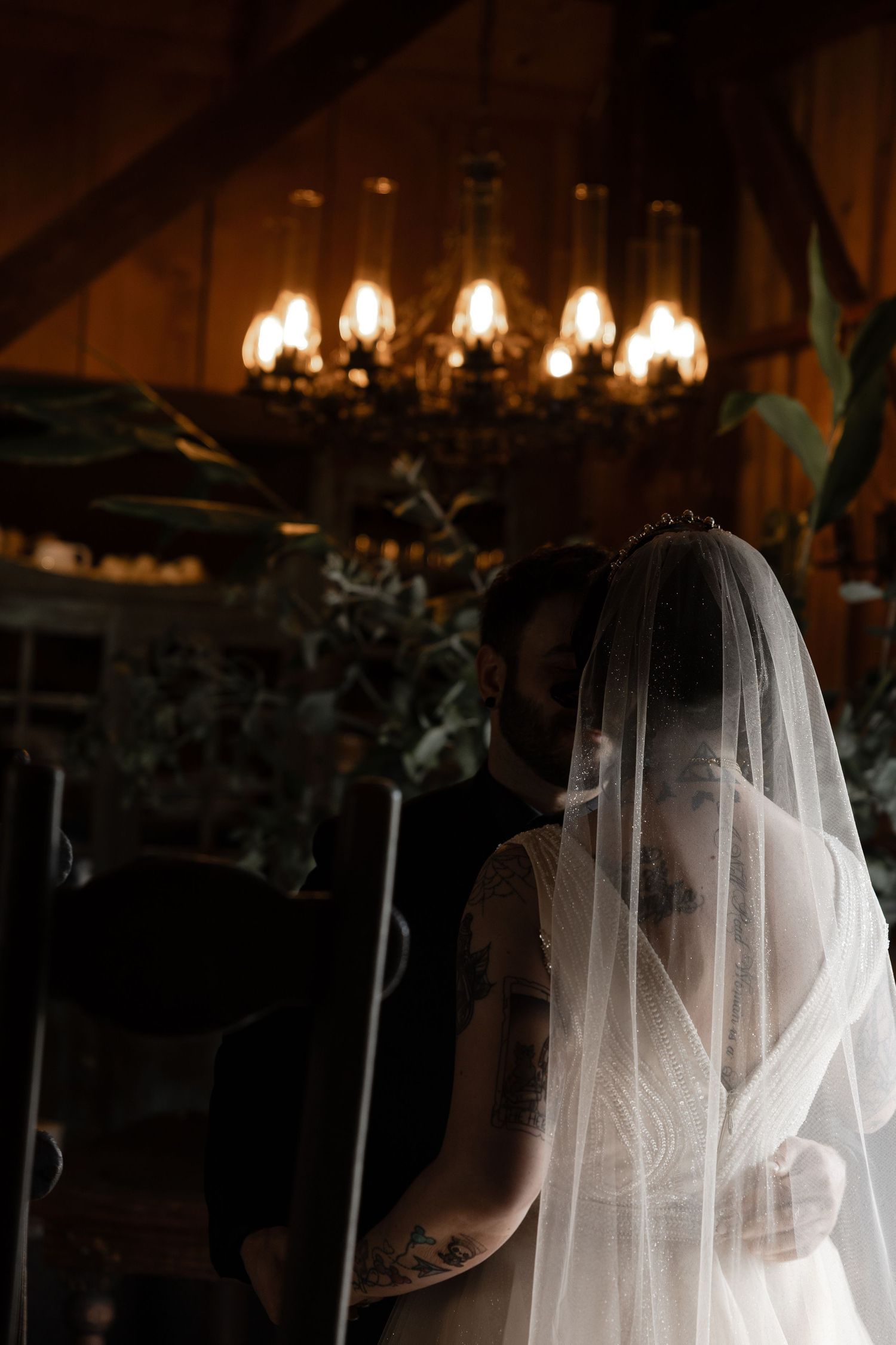 Moody wedding photo with chandelier lighting and a flowing white veil.