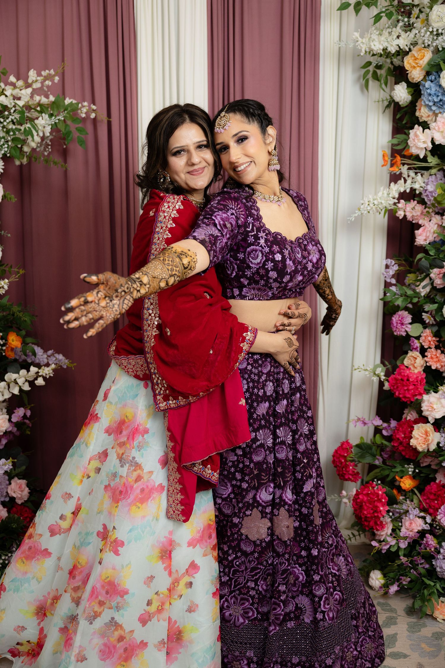 Two outfits shown together - a floral print dress and deep purple formal wear amid floral decorations.