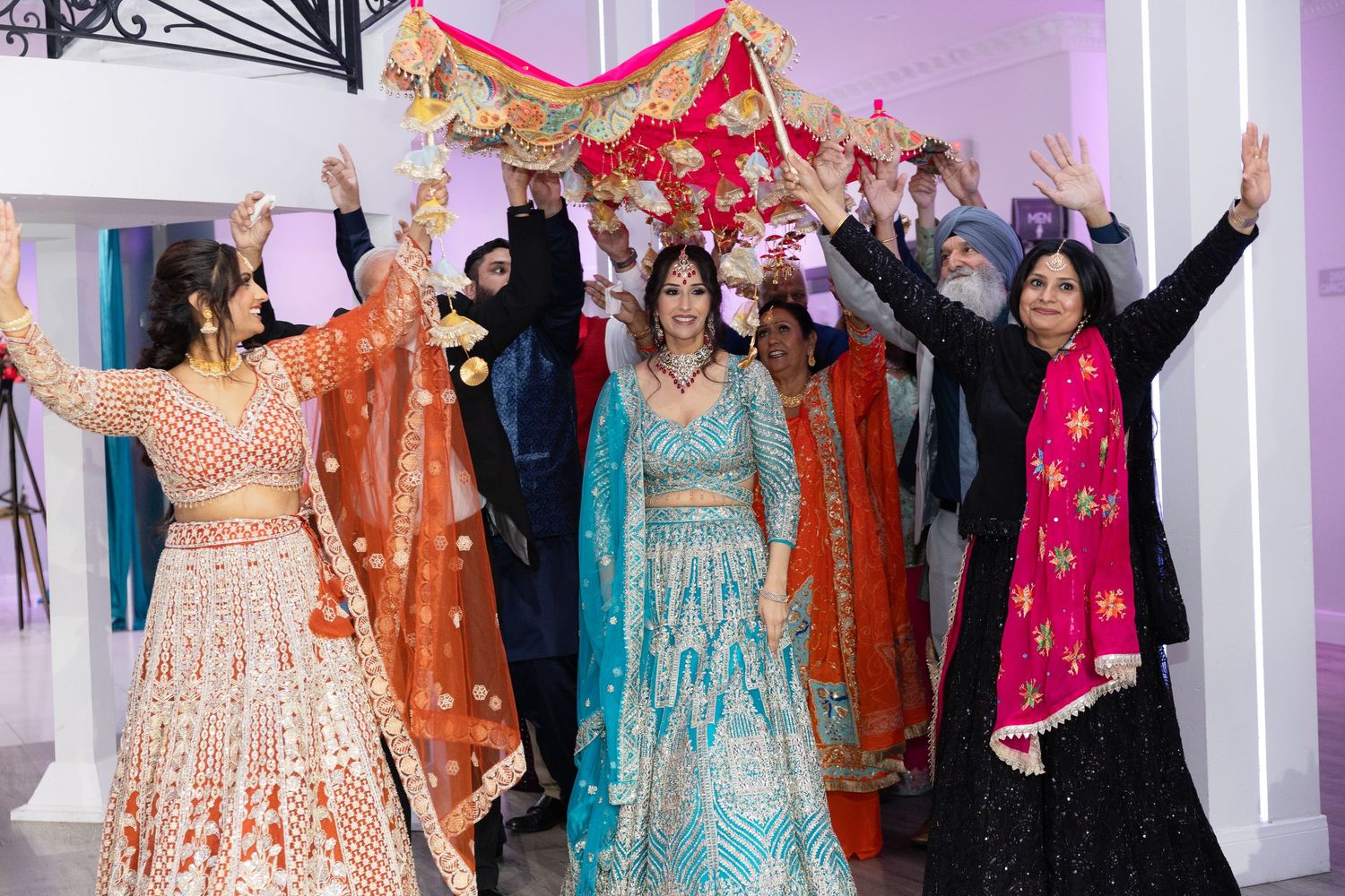 Wedding guests in colorful traditional Indian attire dancing and celebrating at a festive reception party.