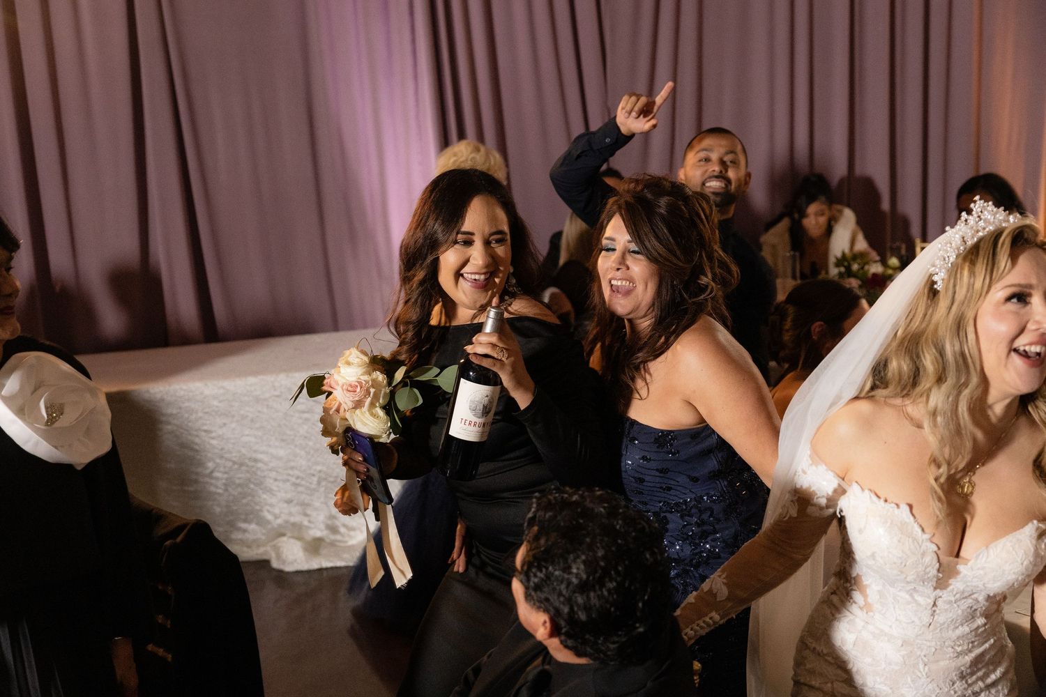 Wedding party dancing and celebrating in a venue with purple curtained walls.