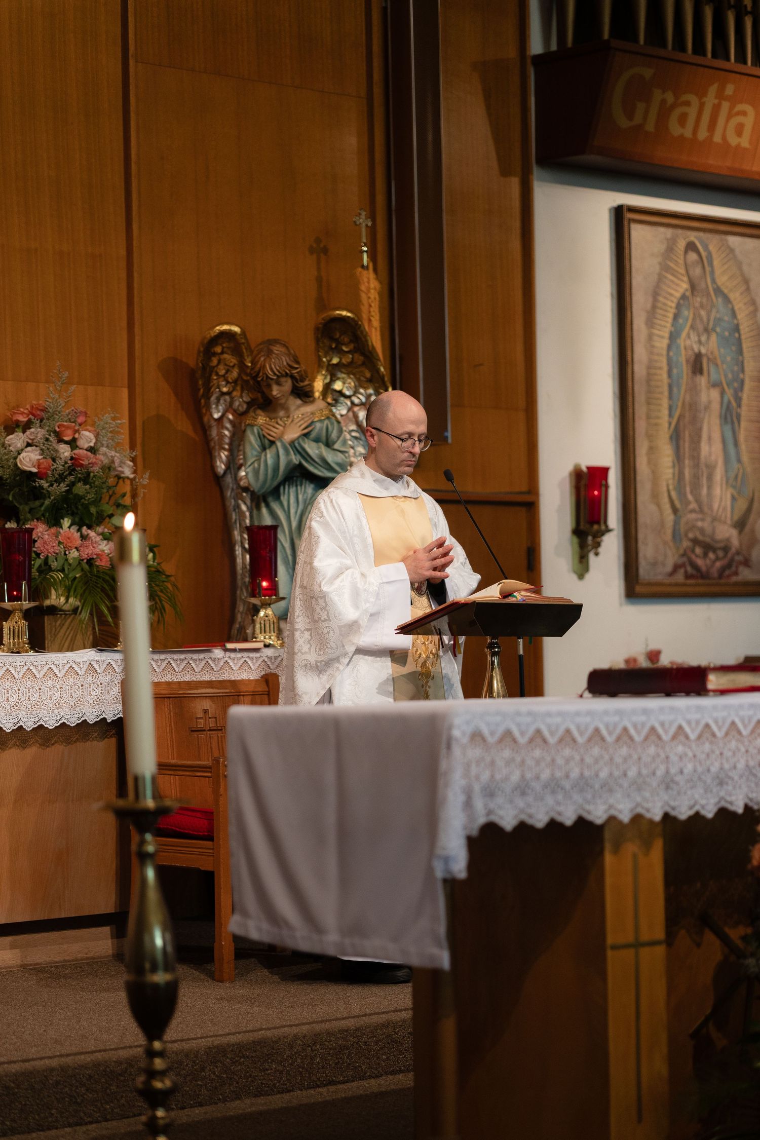 Priest conducting a religious ceremony at an altar decorated with flowers and candles.