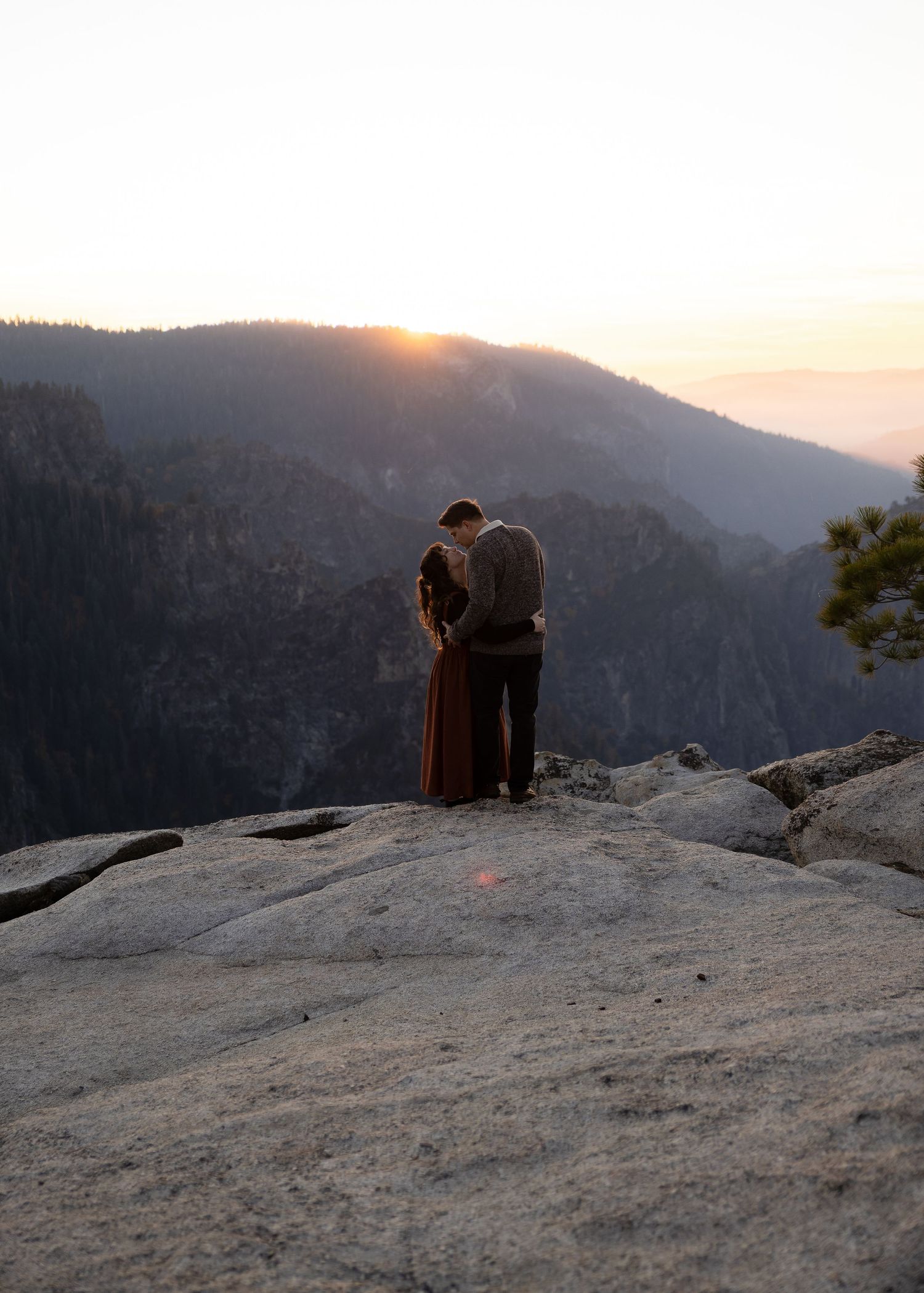 A couple enjoys a peaceful moment on a mountainous overlook during sunset.