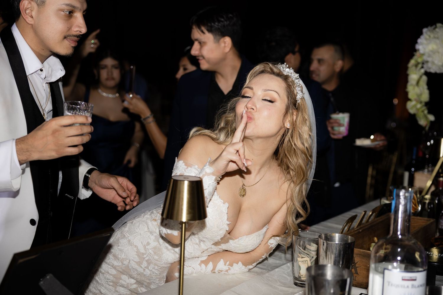 Wedding reception guests enjoying drinks and celebrations in a dimly lit venue.