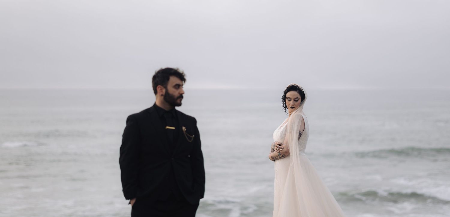 A wedding couple shares a romantic moment against a misty coastal backdrop.