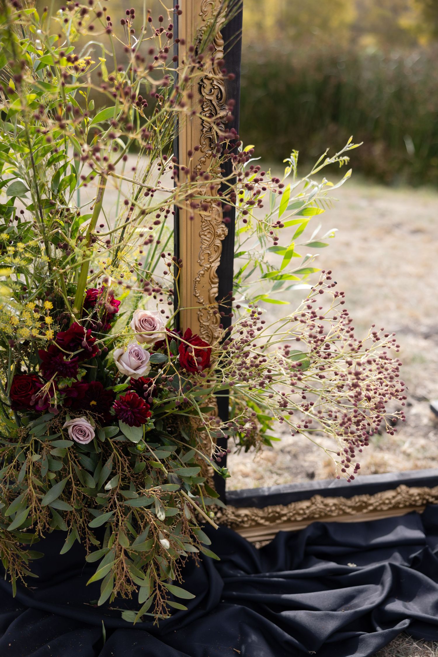 Rustic floral arrangement with deep red roses and delicate greenery against a dark backdrop.
