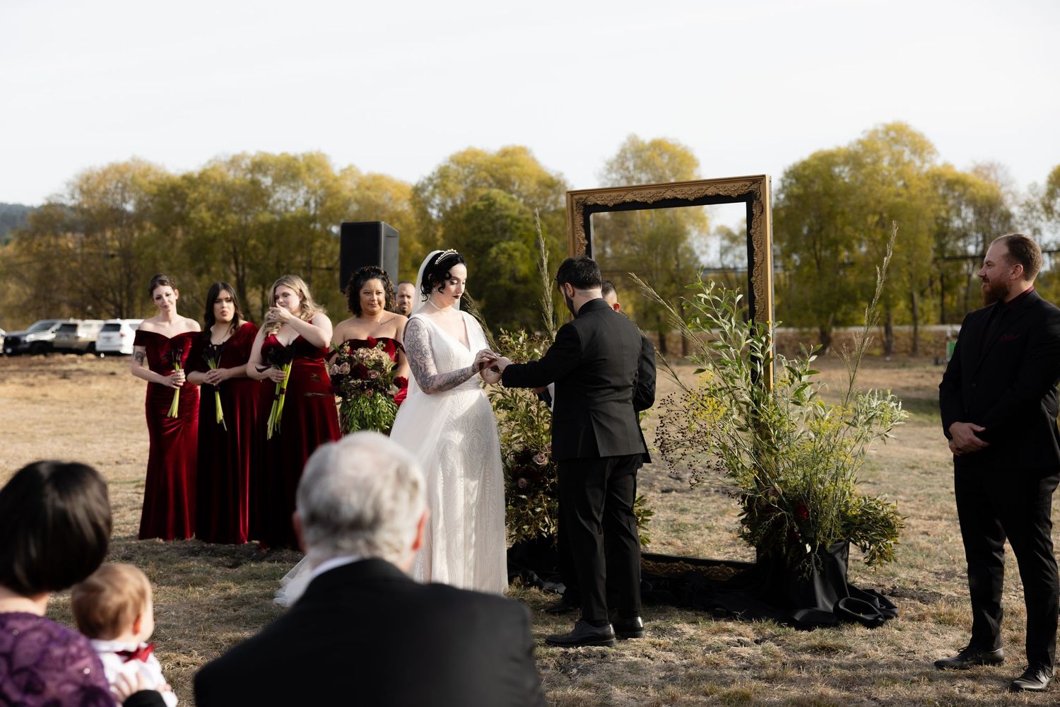 Panoramic view of outdoor wedding ceremony with attendees gathered under autumn trees.