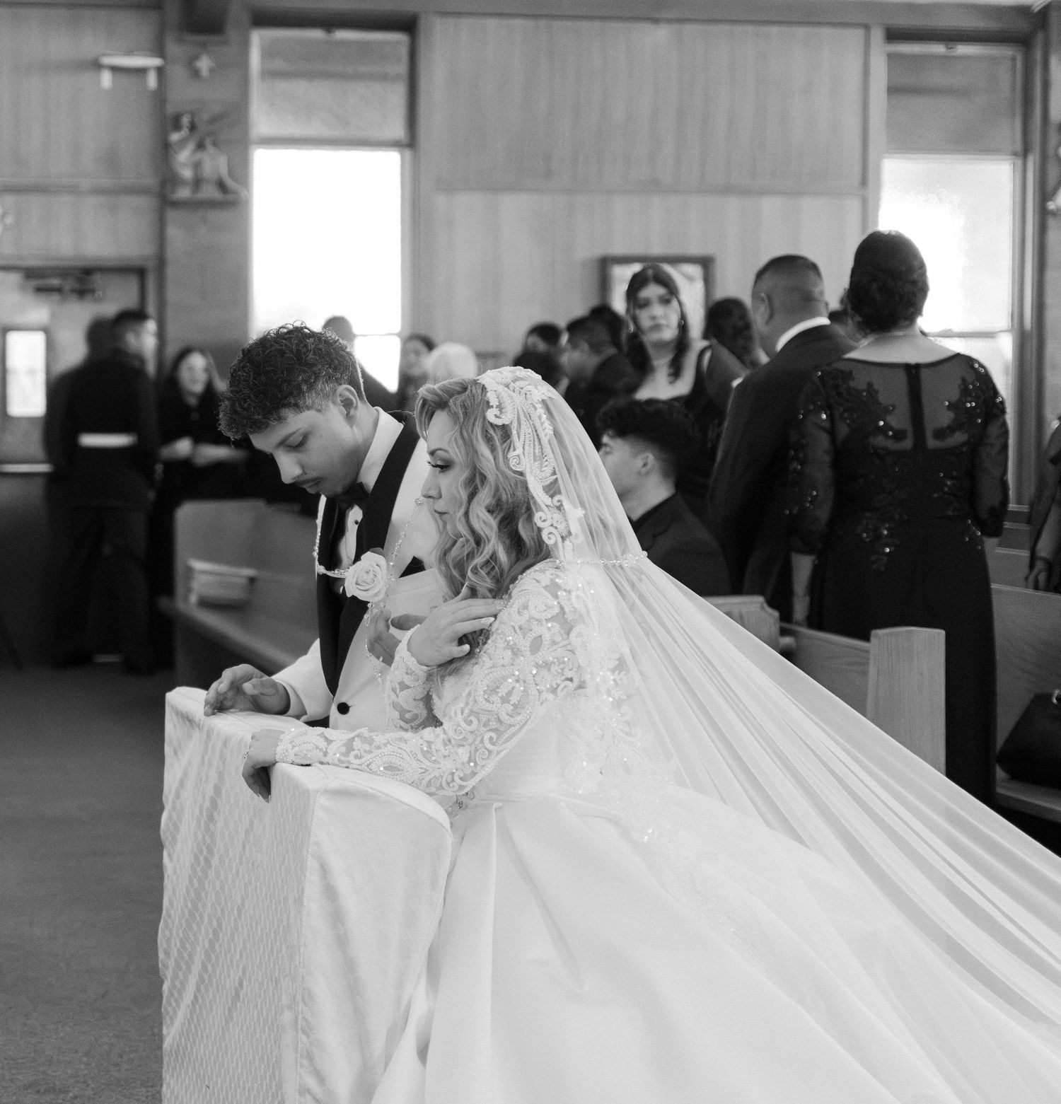 Wedding guests seated in church pews during ceremony with bride in flowing white dress.