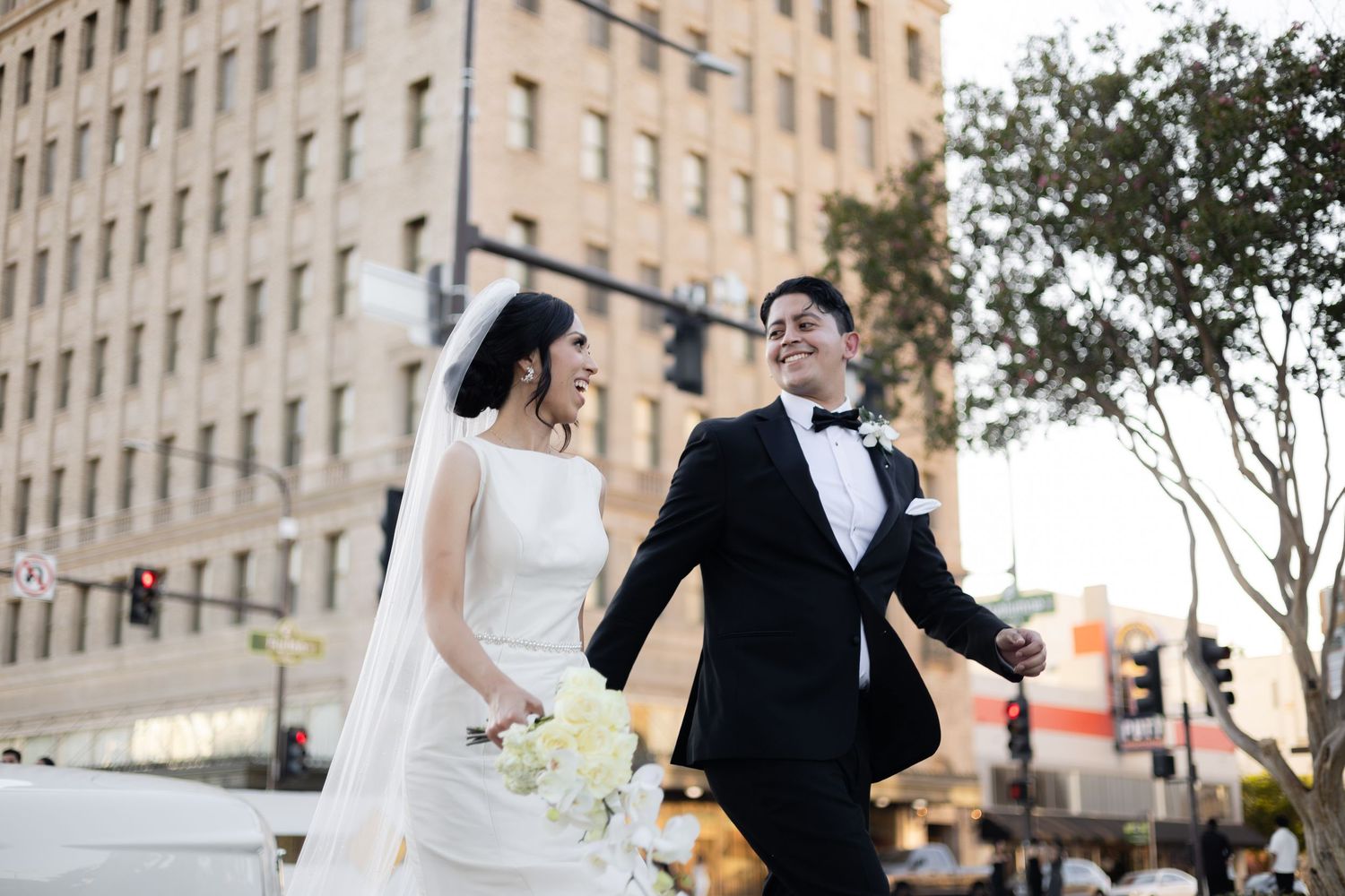 Wedding couple walking and posing for photos outside a grand stone building.