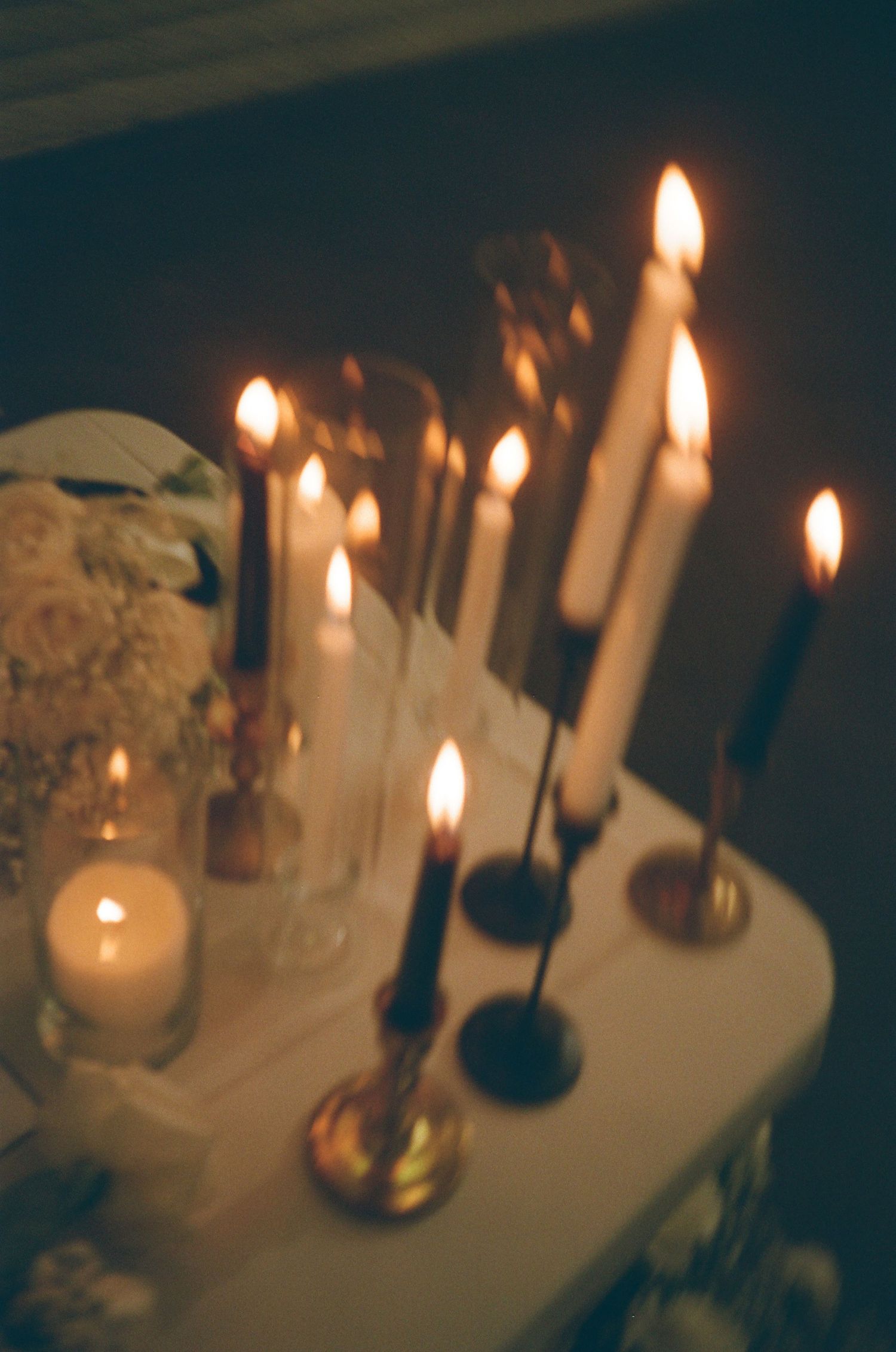 Elegant candlelit display with tall taper candles in gold holders and white floral arrangement on a draped table.