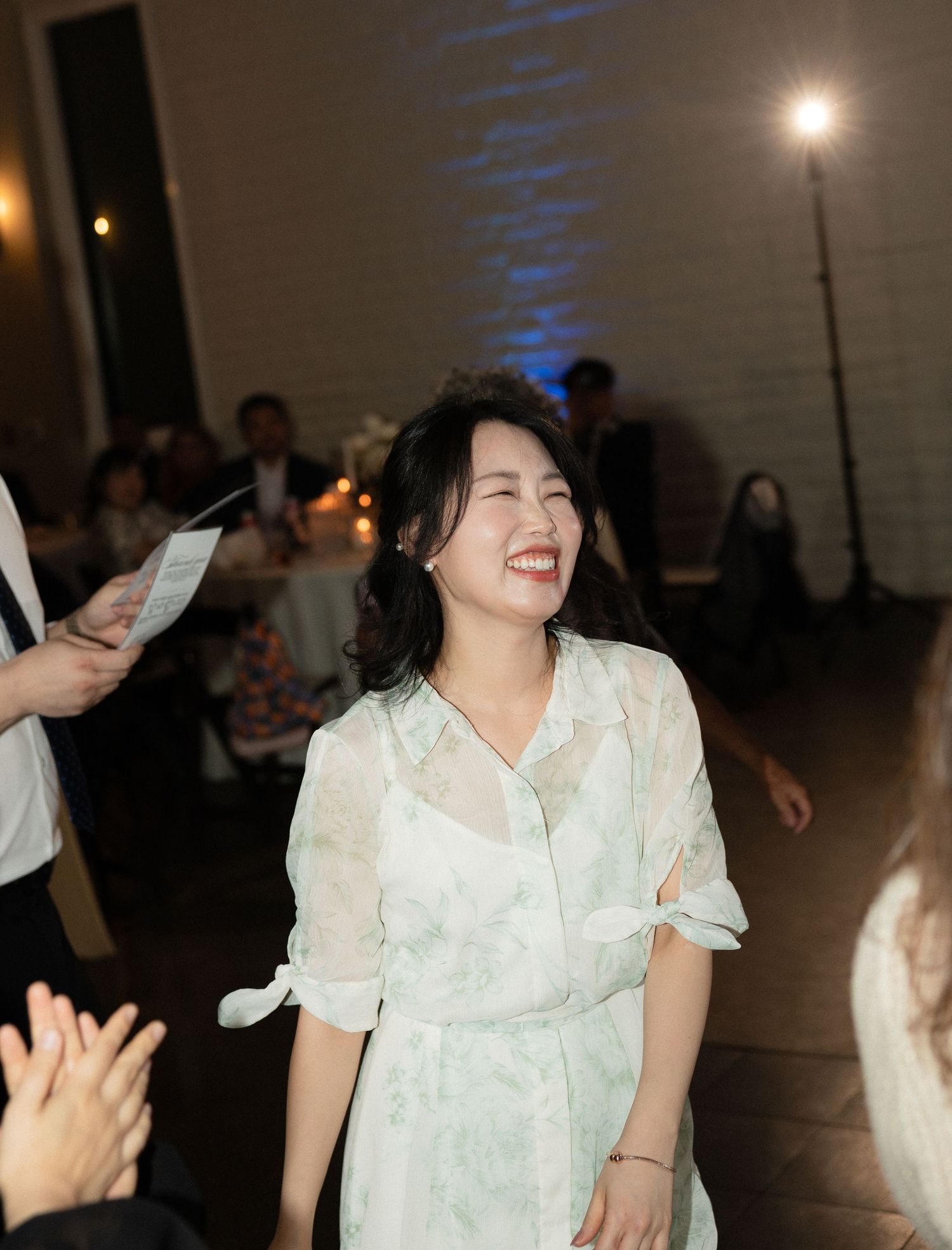 Joyful woman in floral dress laughing at a wedding reception celebration.