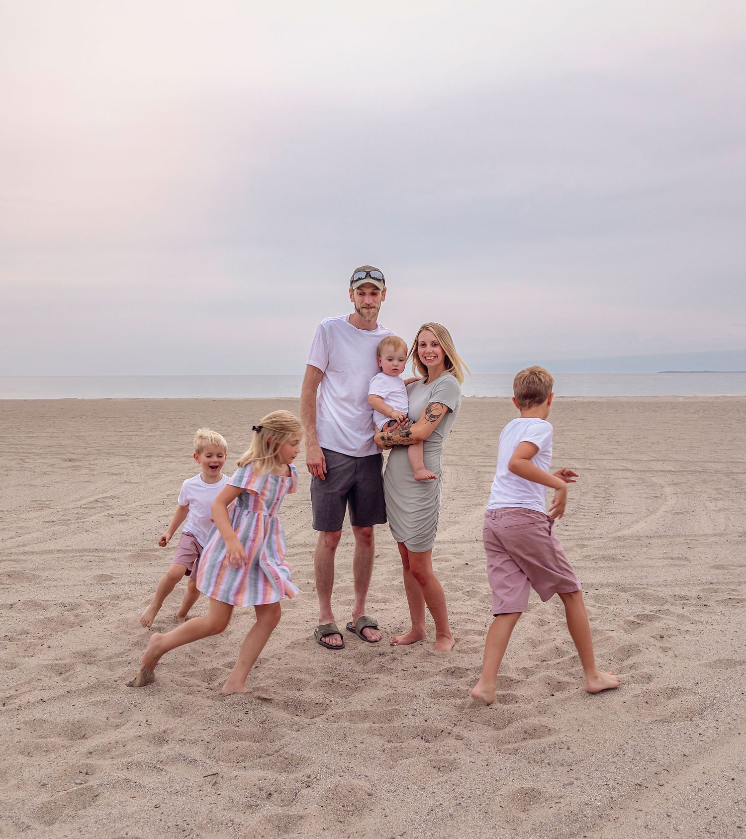 A family enjoys a playful moment together on a sandy beach at sunset.