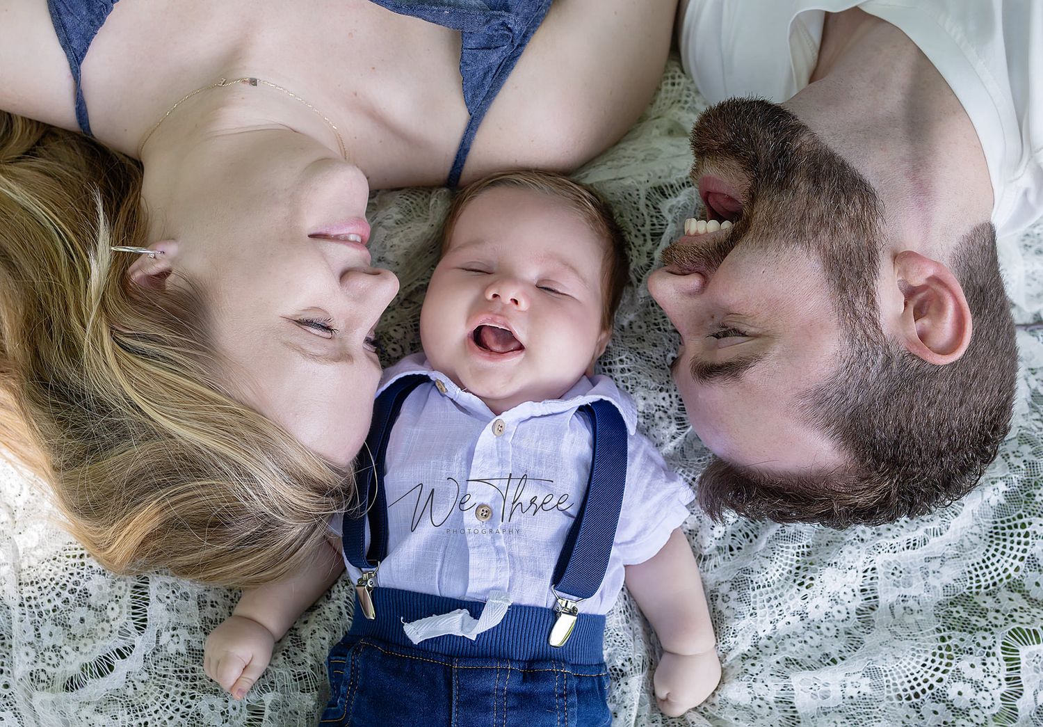 A family lies together on a blanket sharing a joyful moment.