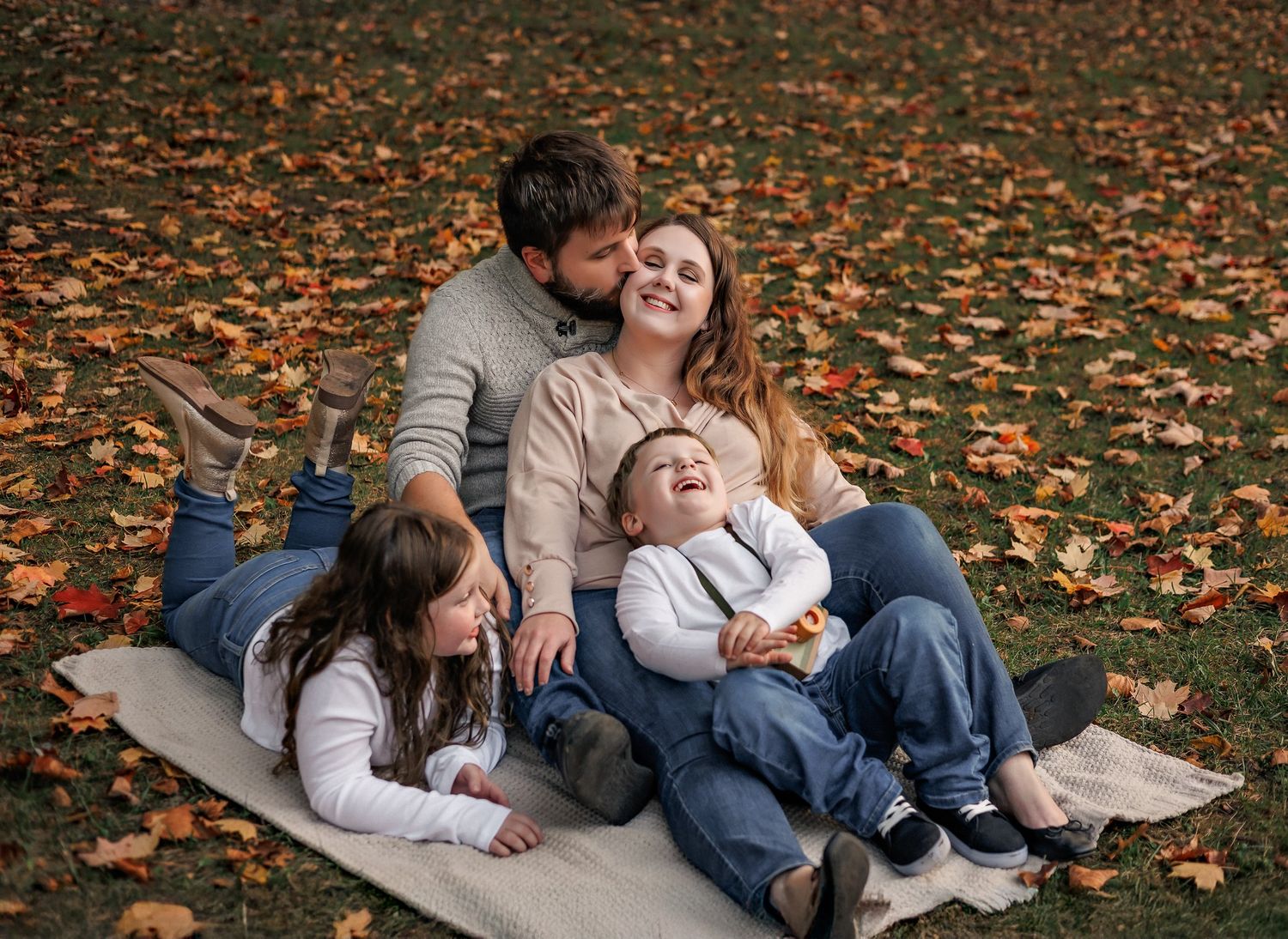 Autumn family photoshoot on ground covered with fallen orange leaves.