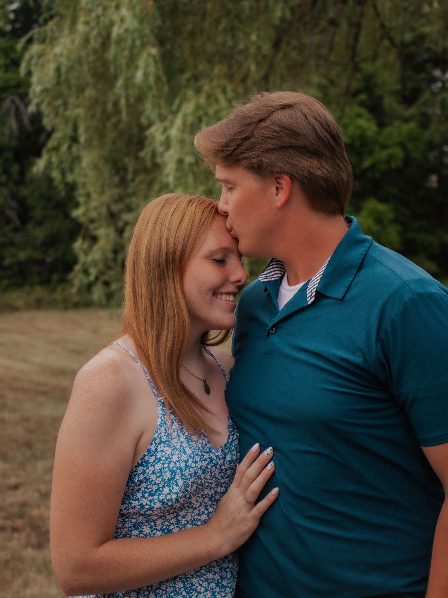 A romantic couple embraces outdoors, with the woman wearing a sparkly blue dress.