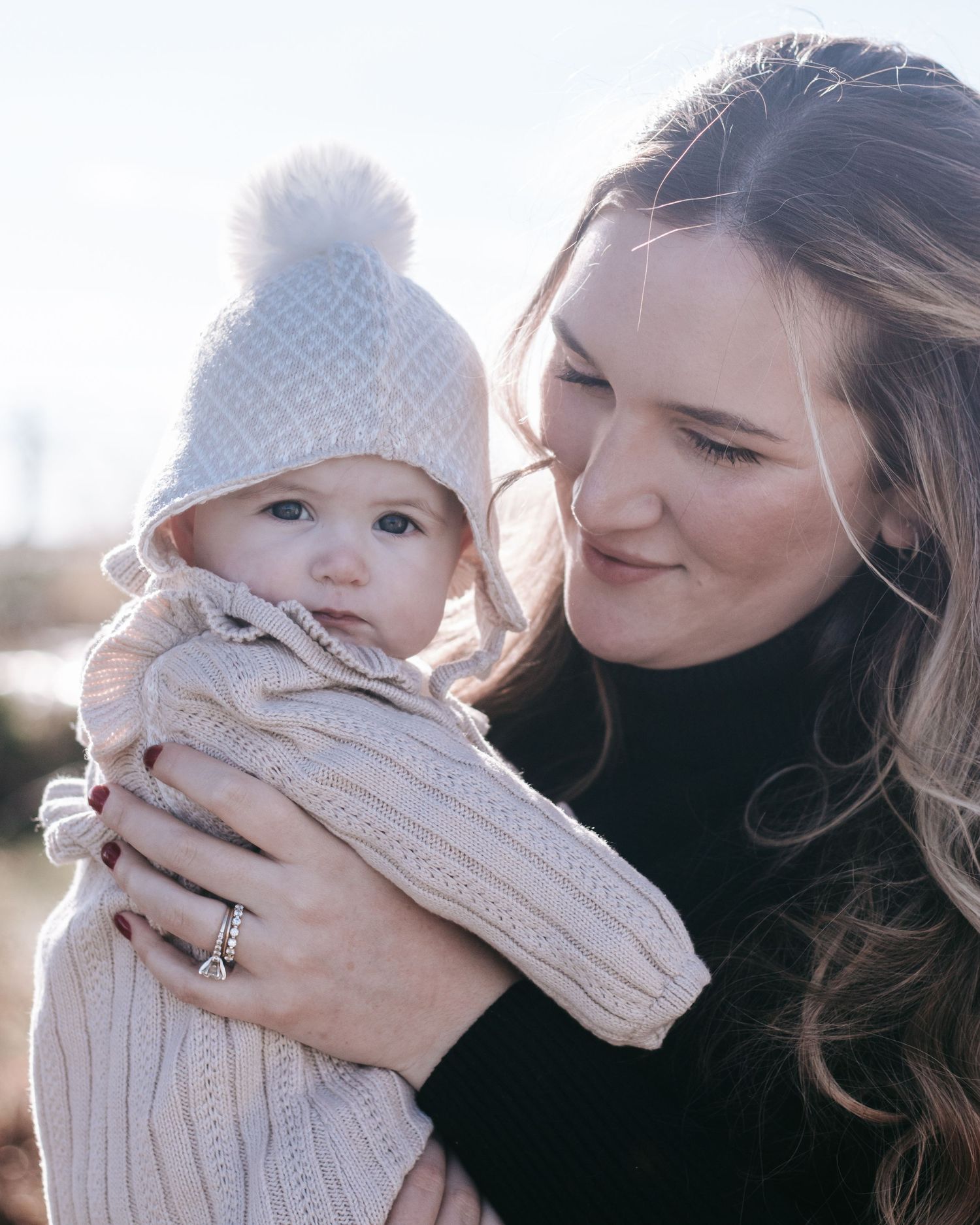 A winter portrait of parent and baby wearing matching knit sweaters and hats in soft lighting.