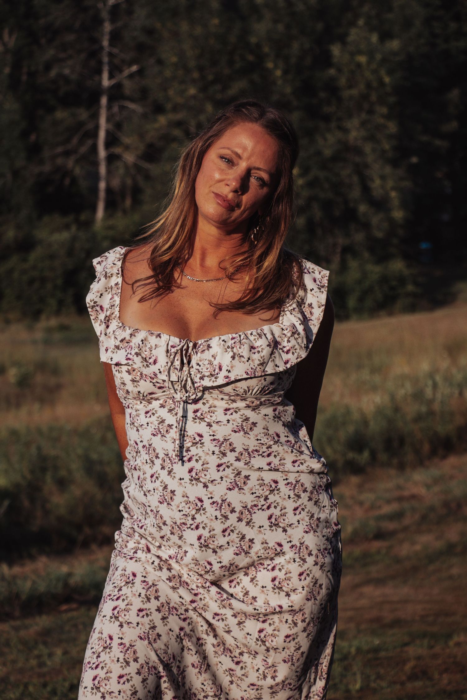 Woman in floral dress posing against natural outdoor backdrop at sunset.