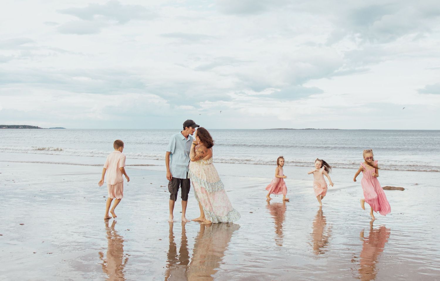 Family enjoying a sunny day at the beach with waves and cloudy sky in background.