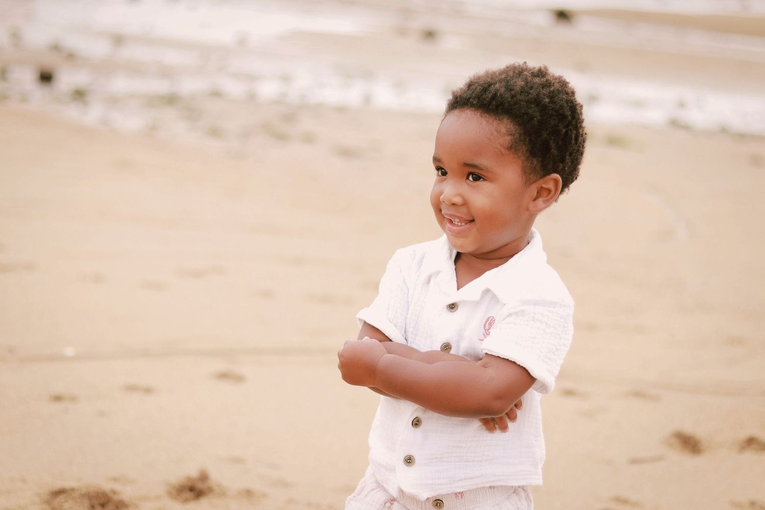 Smiling young child in white shirt standing on sandy beach.