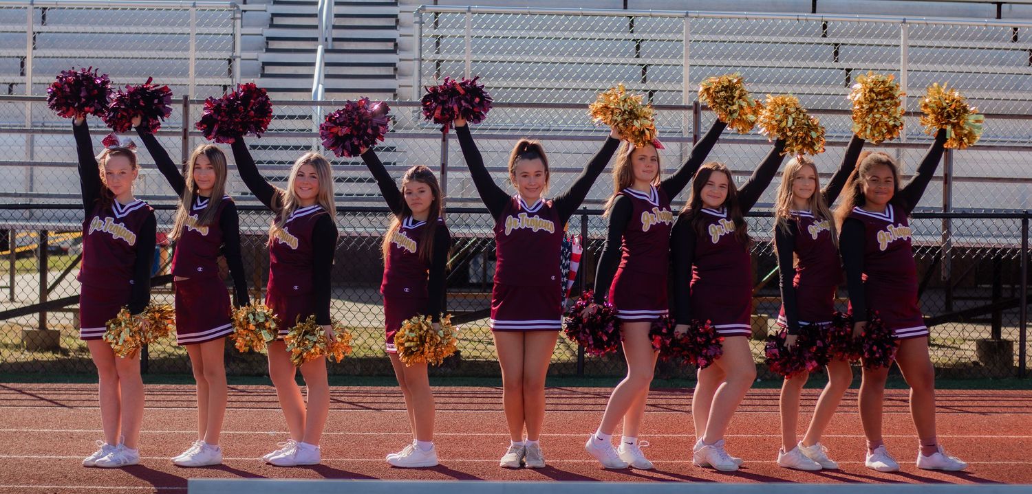 Cheerleaders in maroon uniforms perform in formation on a field holding red and gold pom poms.