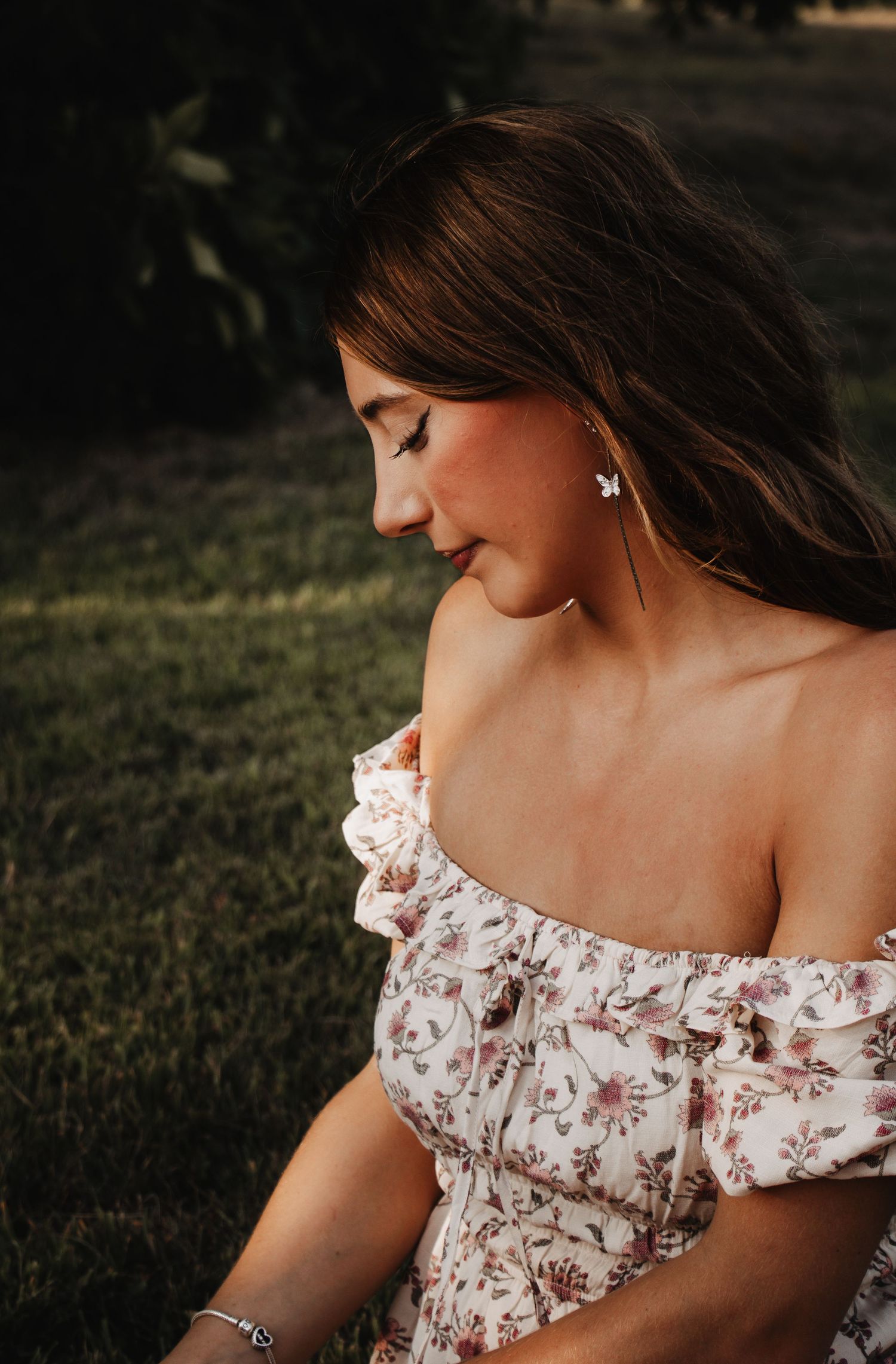 Woman in floral off-shoulder dress posing gracefully in natural outdoor setting.