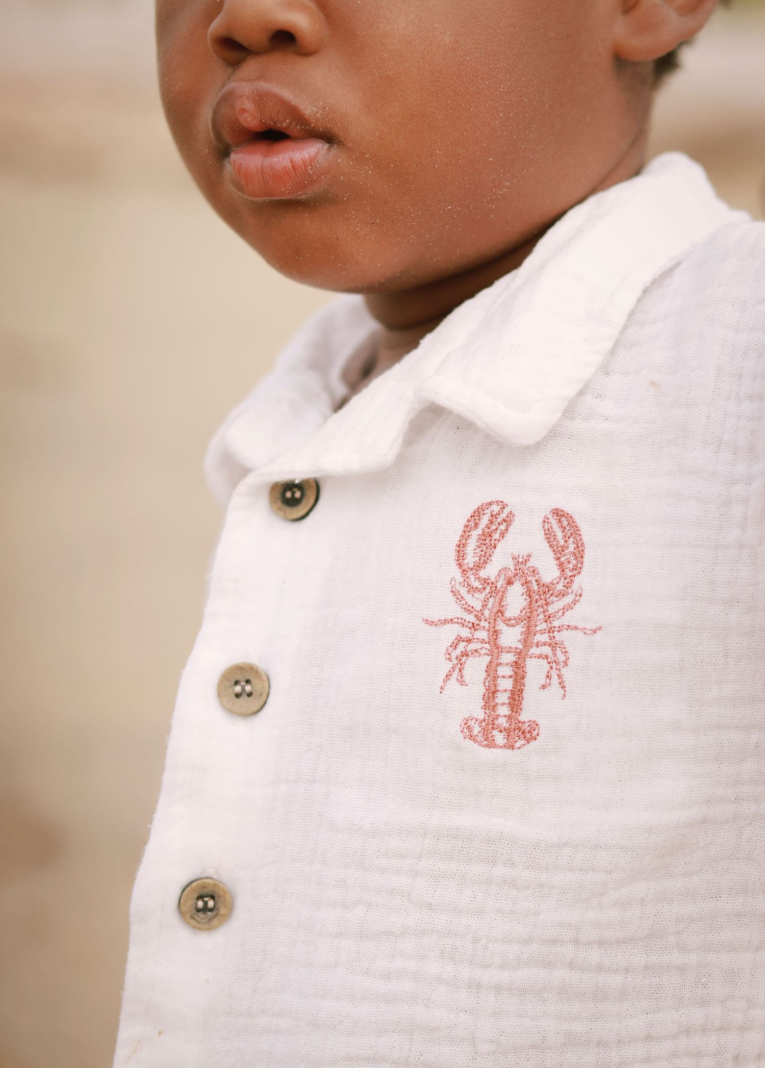 Close-up details of white polo shirts with embroidered red lobster and sea creature designs.