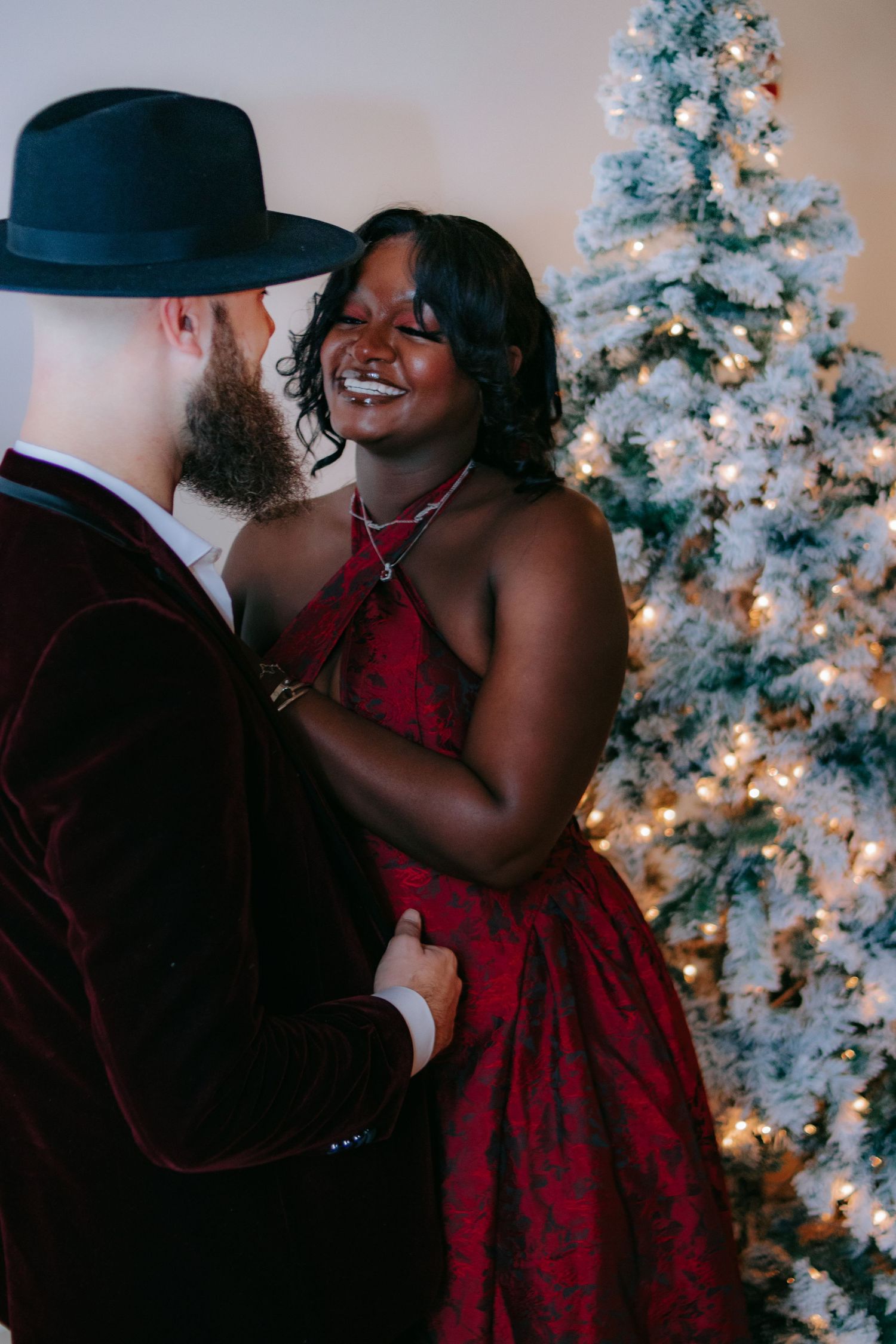 Couple embracing by decorated Christmas tree with twinkling lights.