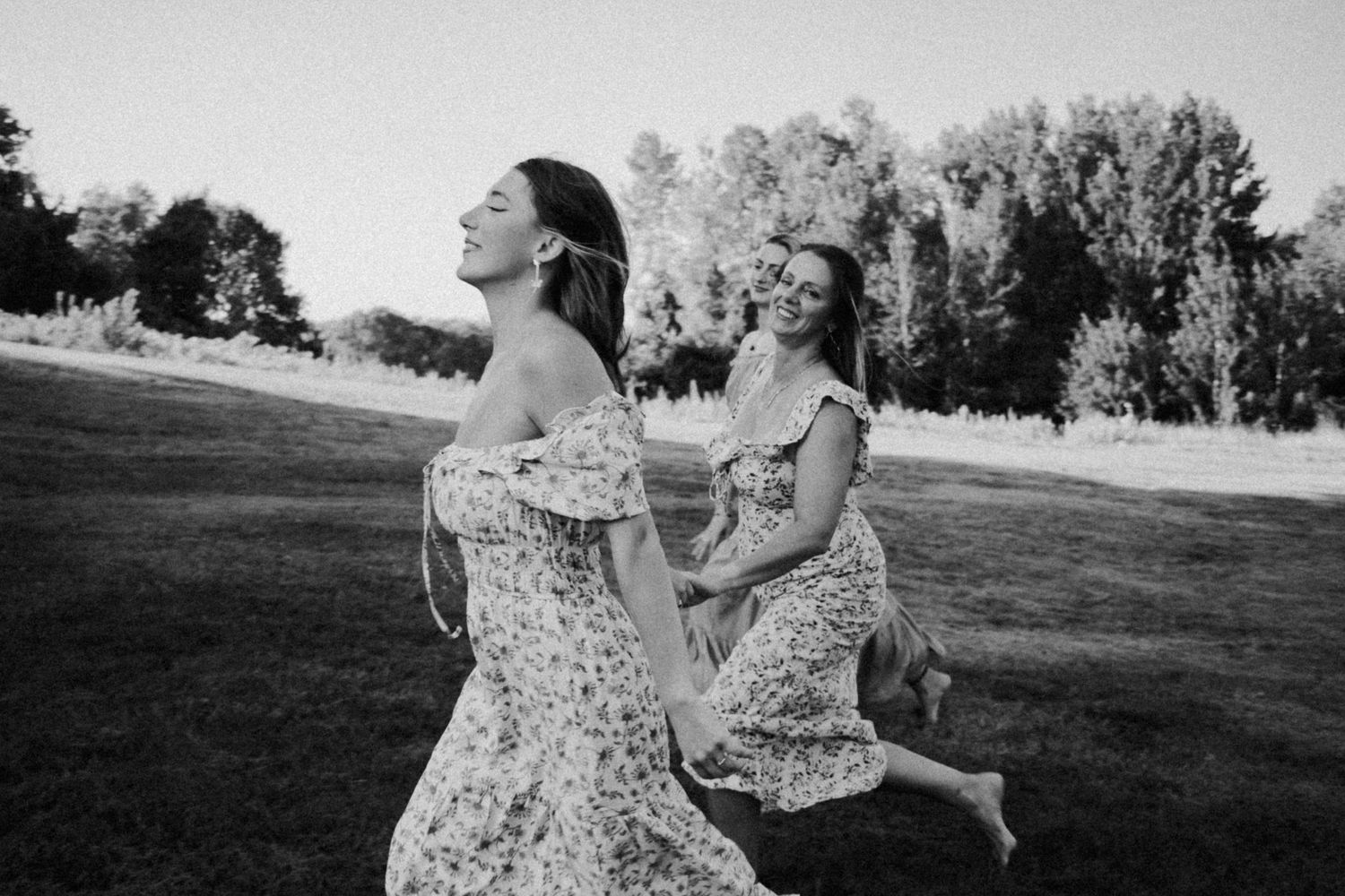 Two people in floral dresses dancing and twirling together in a sunny field.