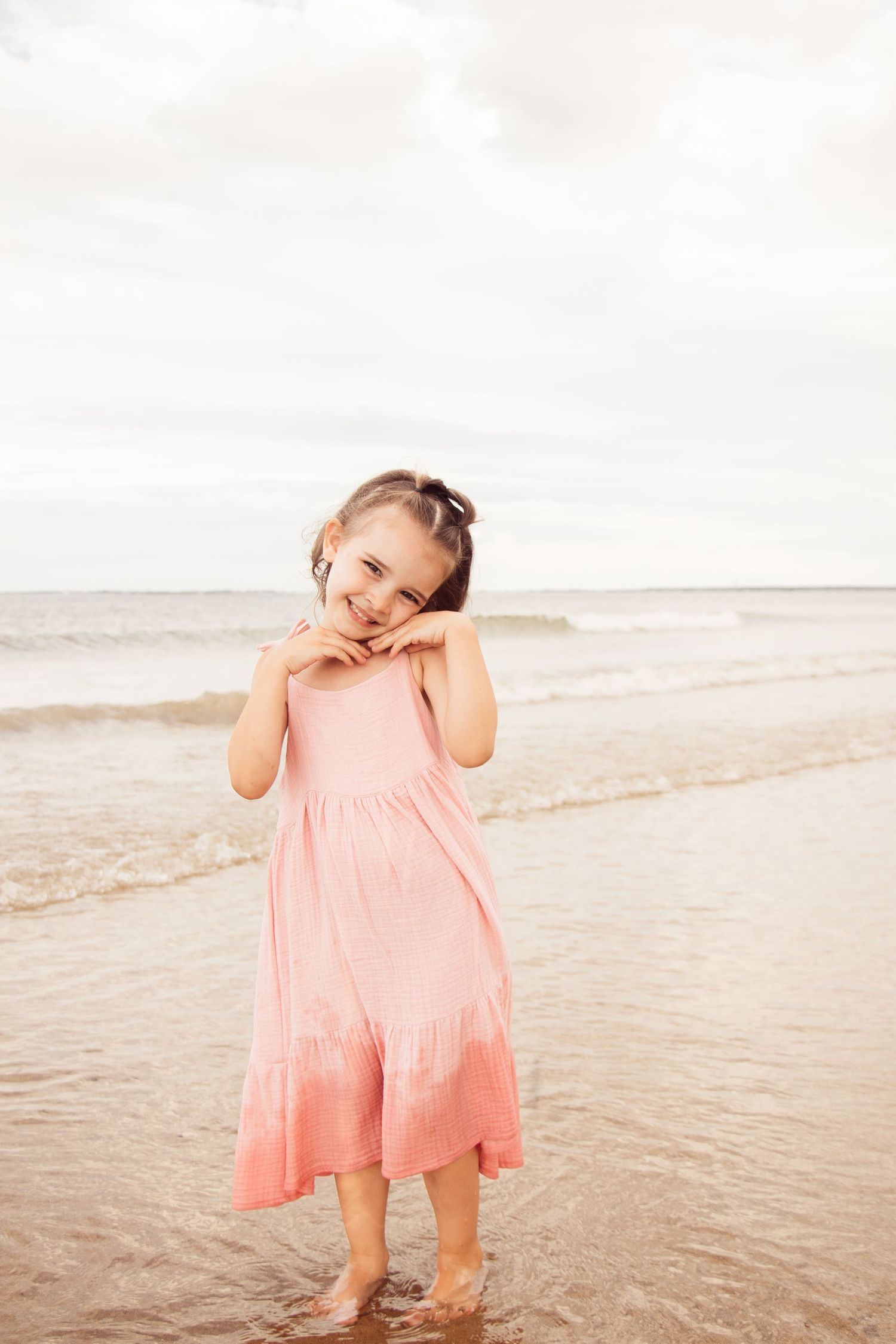 Young person in pink ombre dress playing joyfully at the beach shoreline.