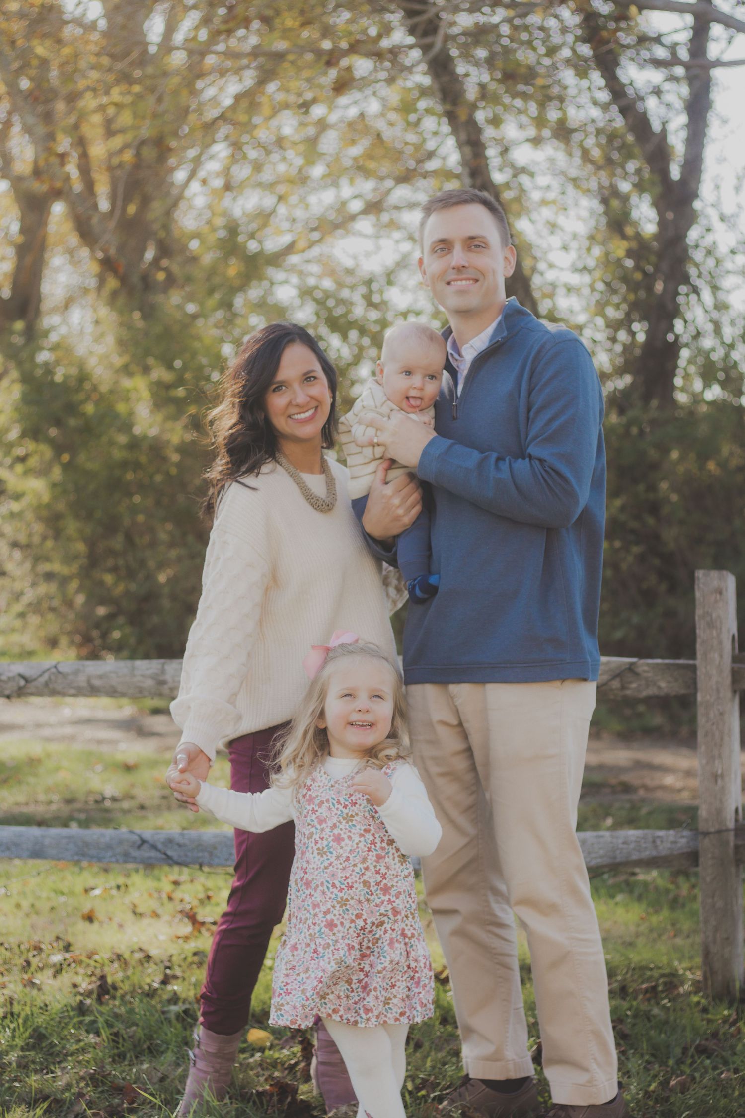 A family poses together outdoors on an autumn day with fall foliage in the background.