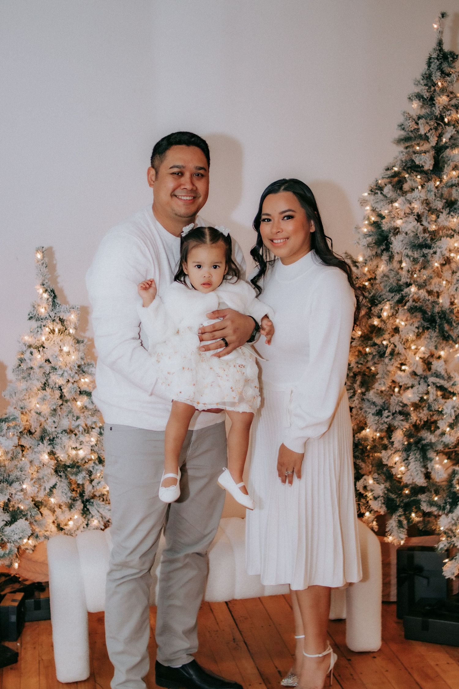 Family in coordinated white outfits poses in front of decorated Christmas tree.