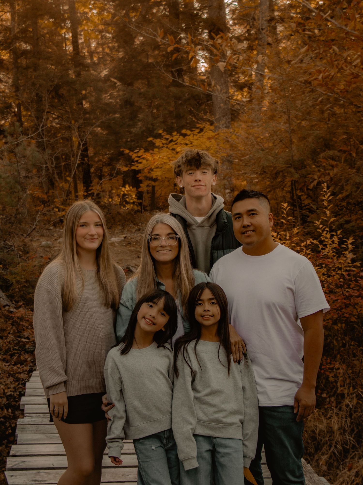 A family group photo on a wooden walkway with fall colors in the background.