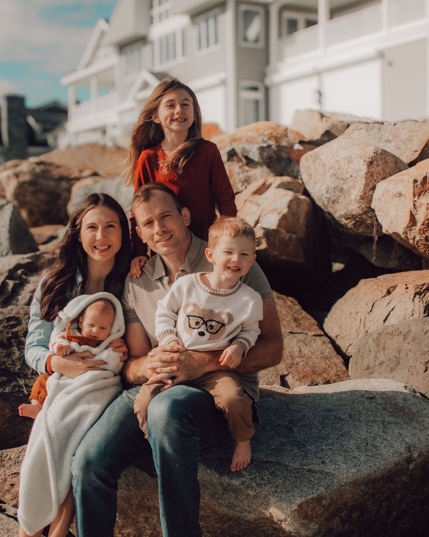Family sitting together on rocky beach during sunset with ocean view.