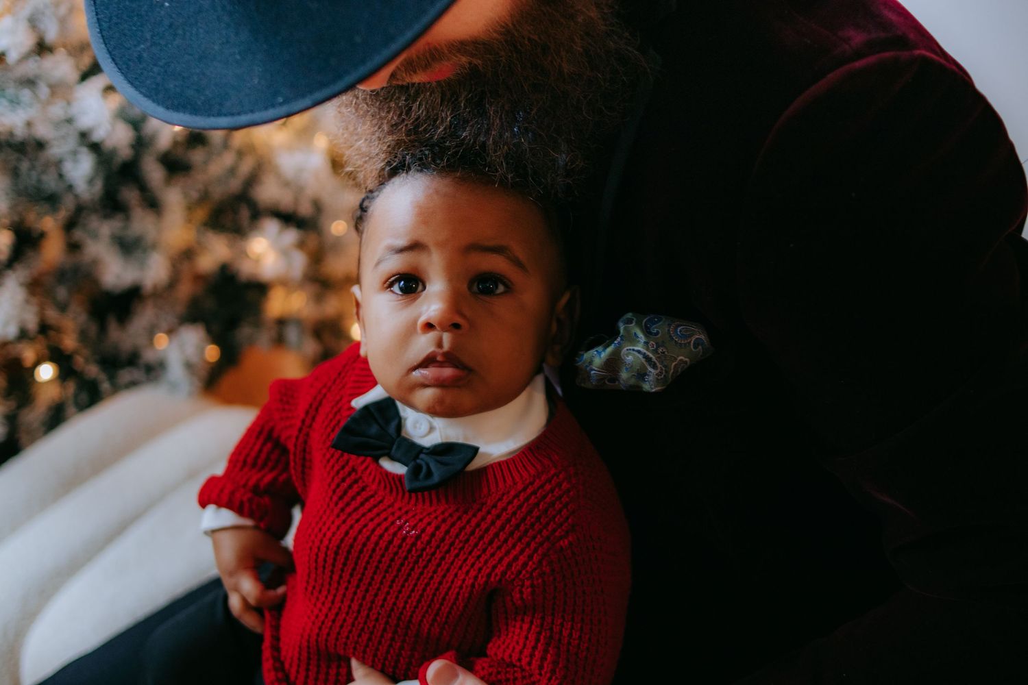 Child in red sweater during holiday photoshoot with Christmas tree in background.