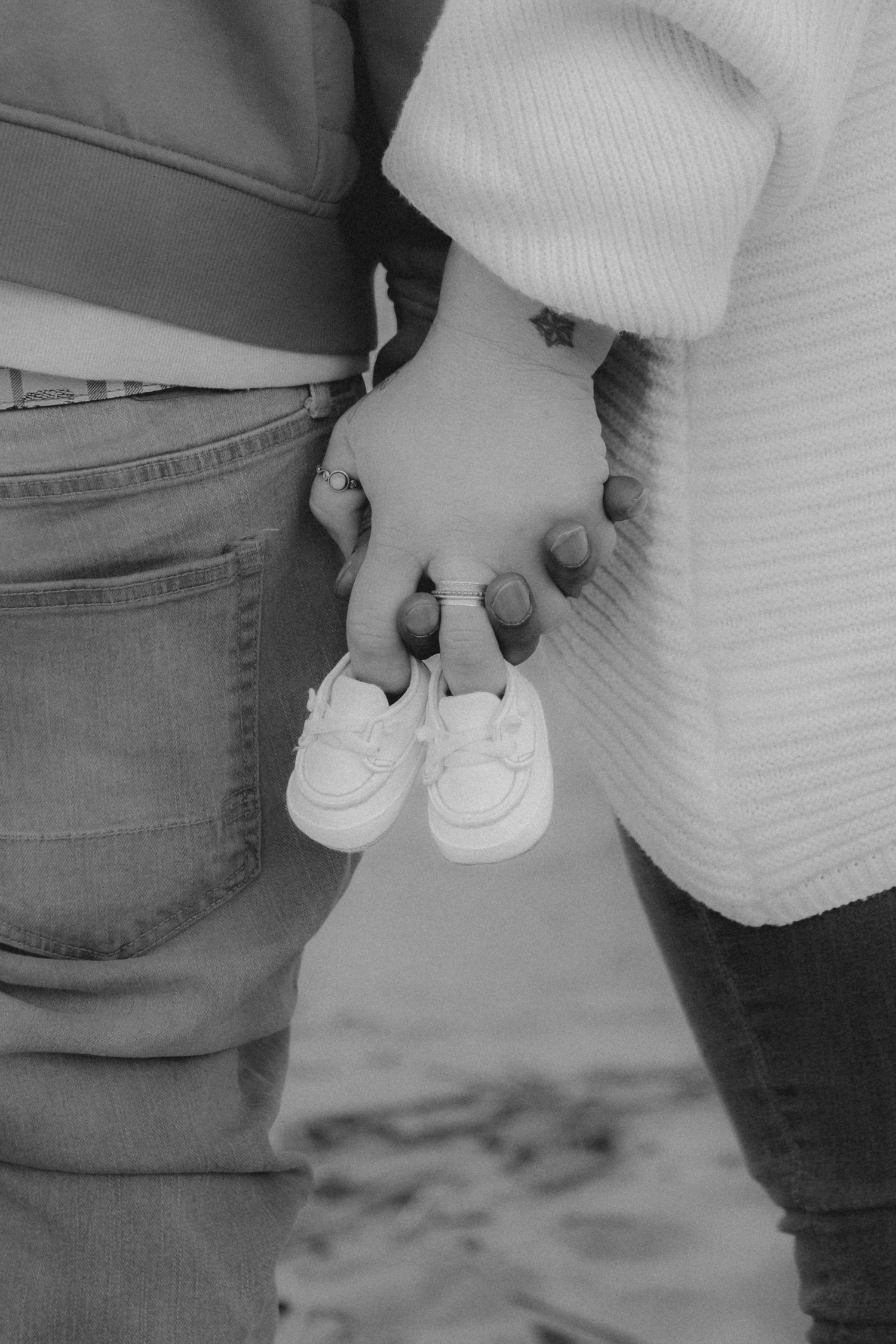 Black and white photo of couple holding hands and tiny baby shoes, announcing pregnancy.