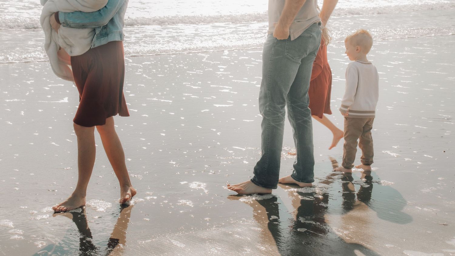 Cropped view of people's feet walking along a sandy beach shoreline.
