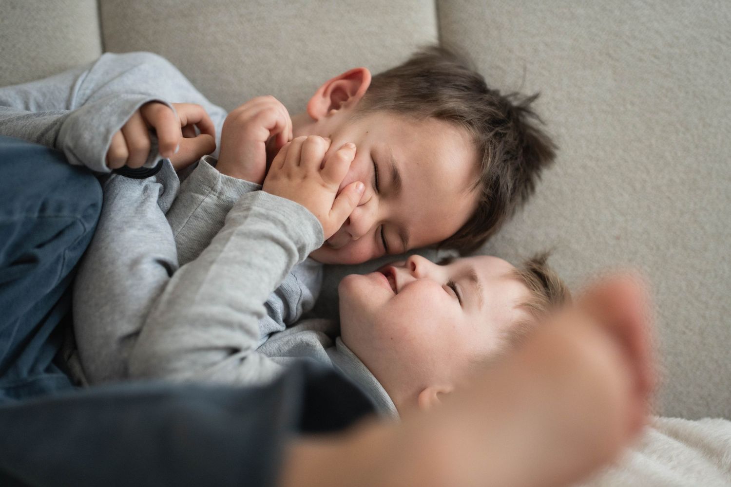 Intimate close-up shots of playful moments on a light colored couch.
Deux petits garçons chahutant et riant sur le canapé.