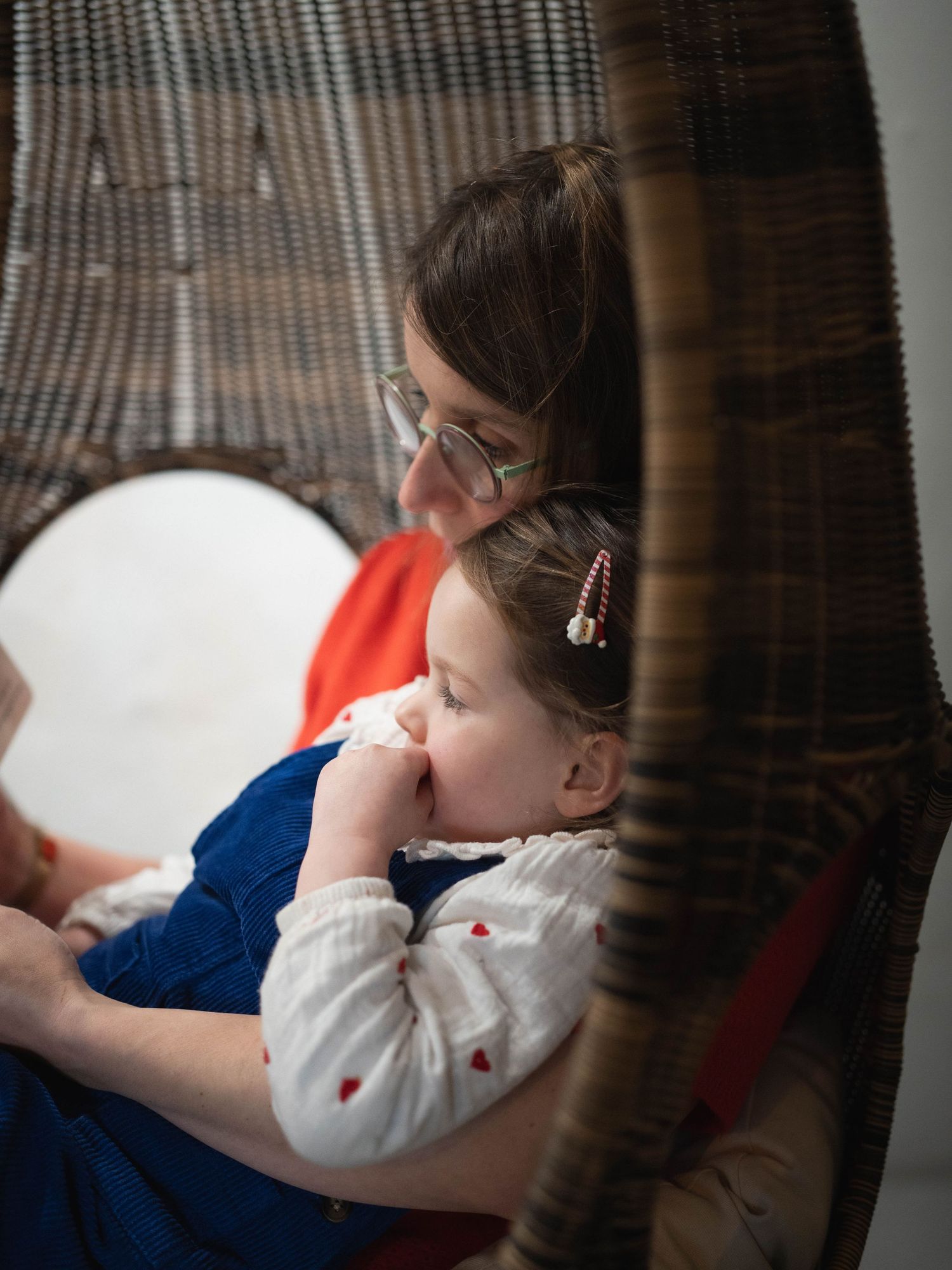 Child resting on couch wearing white blouse with decorative pattern visible.
Maman lisant un livre à sa fille dans ses bras.