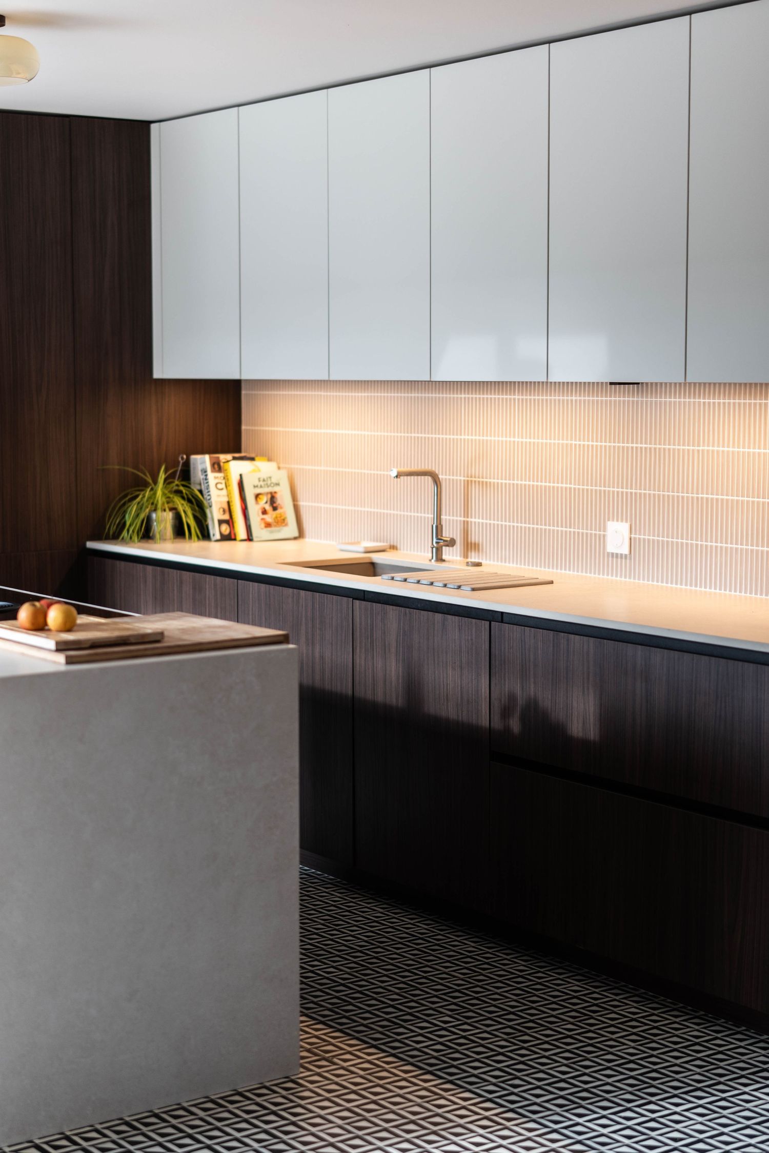 Contemporary kitchen design featuring white upper cabinets and dark base units with textured flooring.
Cuisine contemporaine.