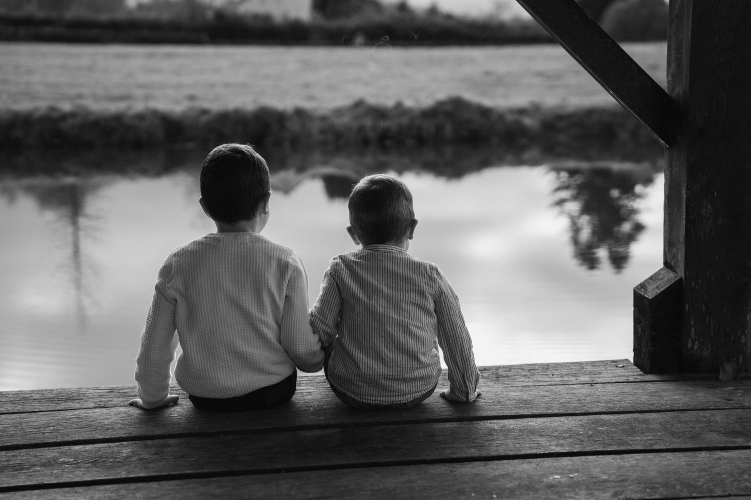 Silhouettes sitting by water at sunset in a peaceful moment.
Photo en noir et blanc de deux enfants assis au bord de l'eau.