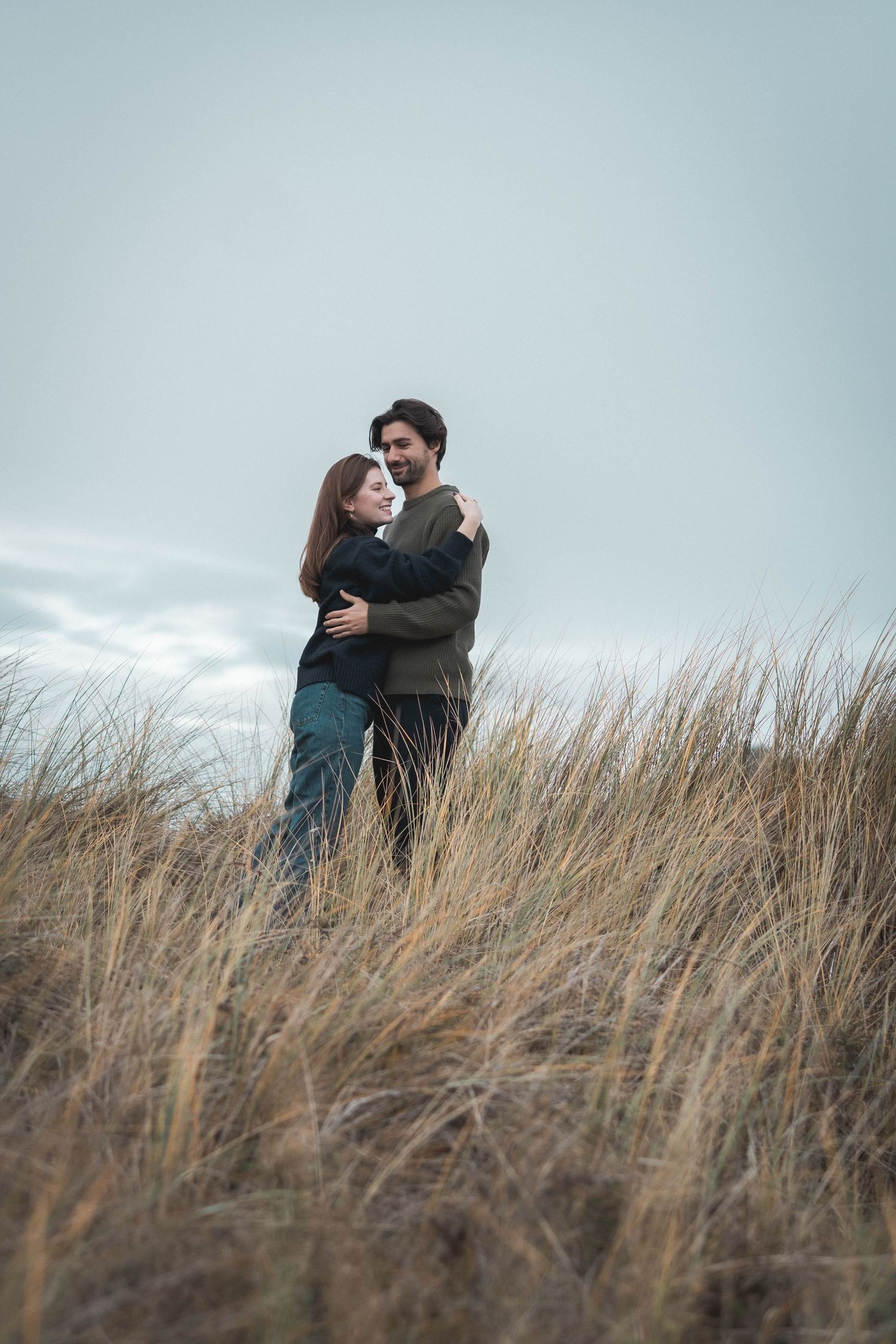 Two people hugging in tall beach grass during golden hour.
Couple qui se prend dans les bras dans les herbes hautes.