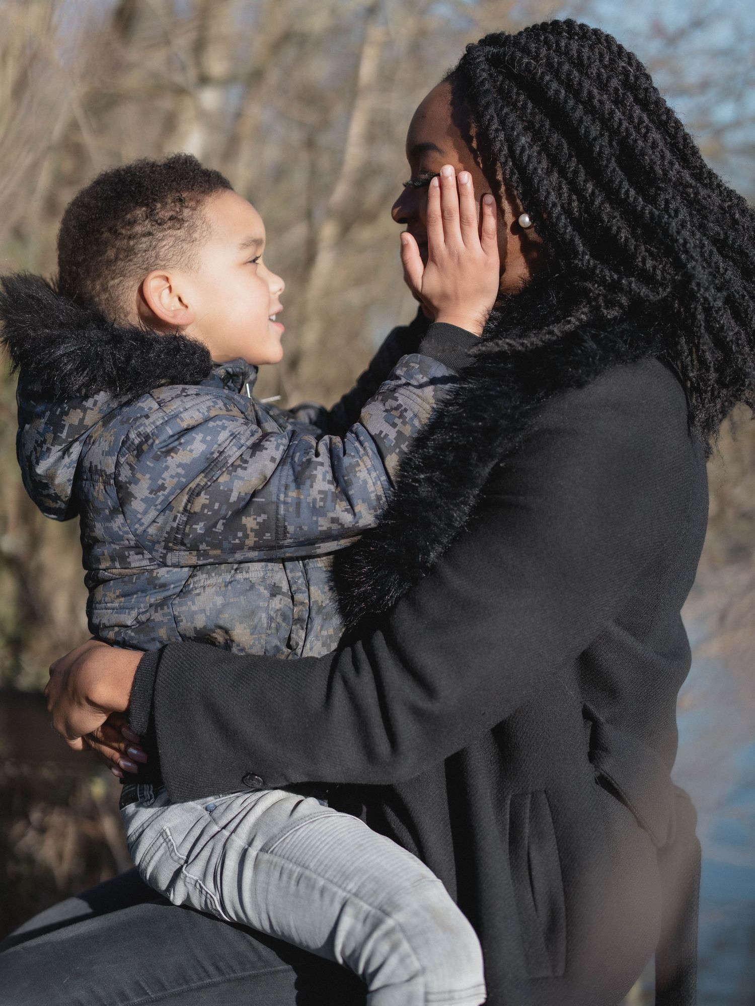 Tender moment captured between two people embracing by a lake with bare trees in background.
Câlin entre une mère et son fils dans la nature