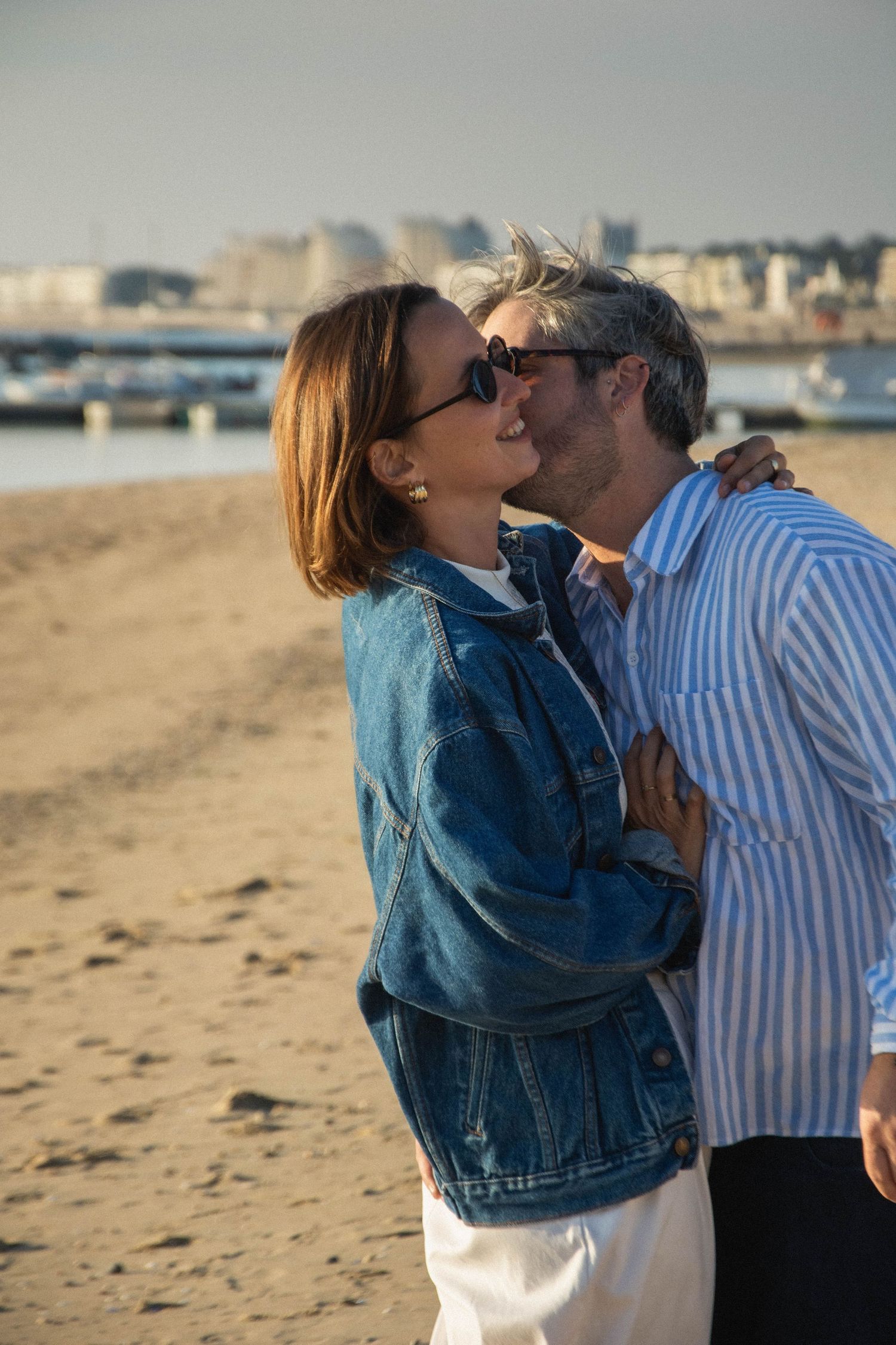 A tender moment between a couple sharing a kiss on a sunny beach.