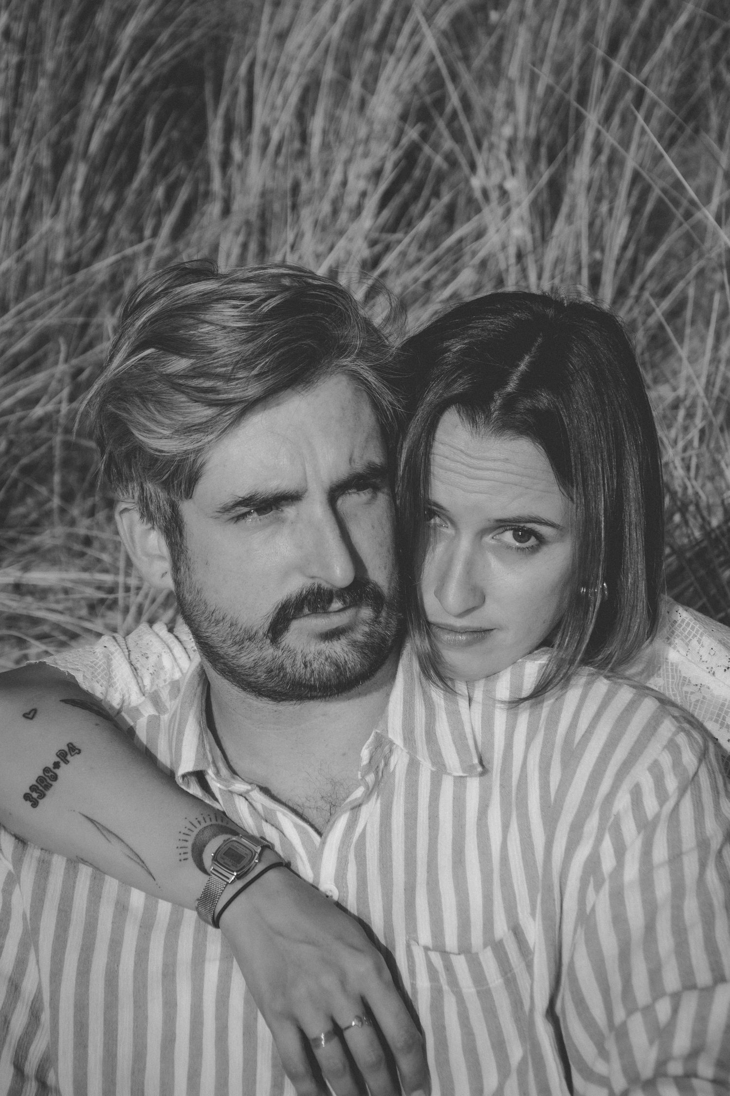 Black and white portrait of couple lying in tall grass.
Photo en noir et blanc d'un couple qui s'enlace dans les herbes hautes.