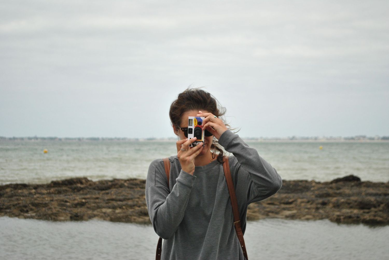 Person taking photographs at a coastal location on an overcast day.
Personne à la mer prenant une photo avec un appareil photo jetable.